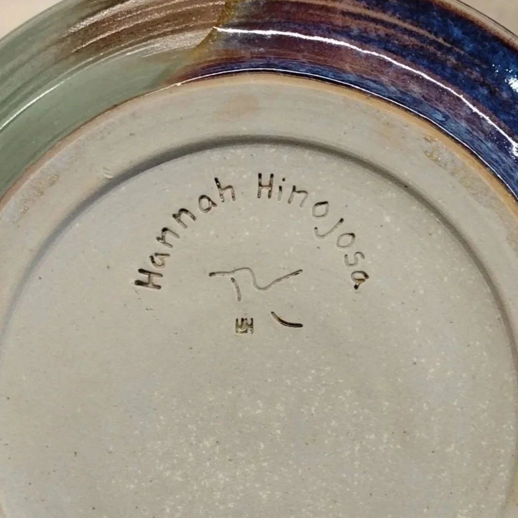 Close-up of the bottom of a ceramic plate with the inscription 'Hannah Hinojos' and a signature.