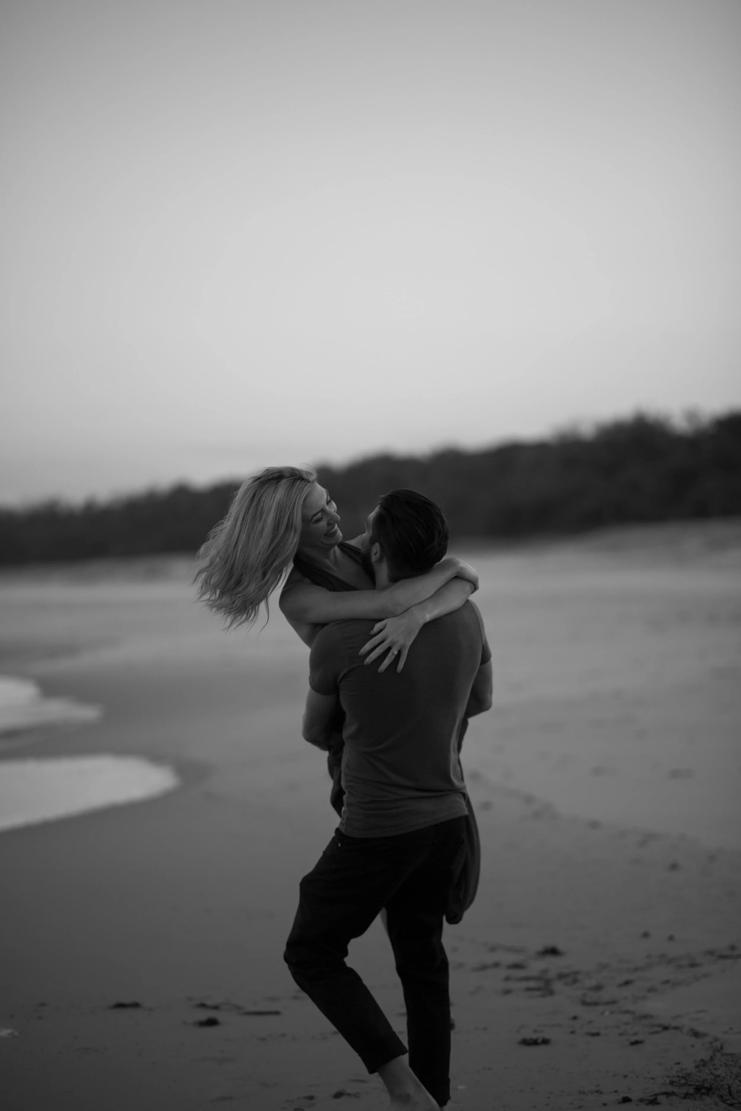 Couple showing affection while spinning around and lifting the other on Fingal beach. 