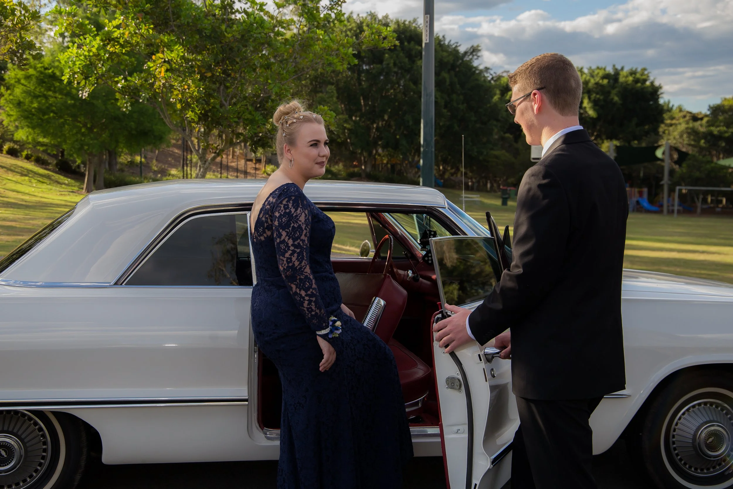 Male holds open car door for female in natural golden light setting. 