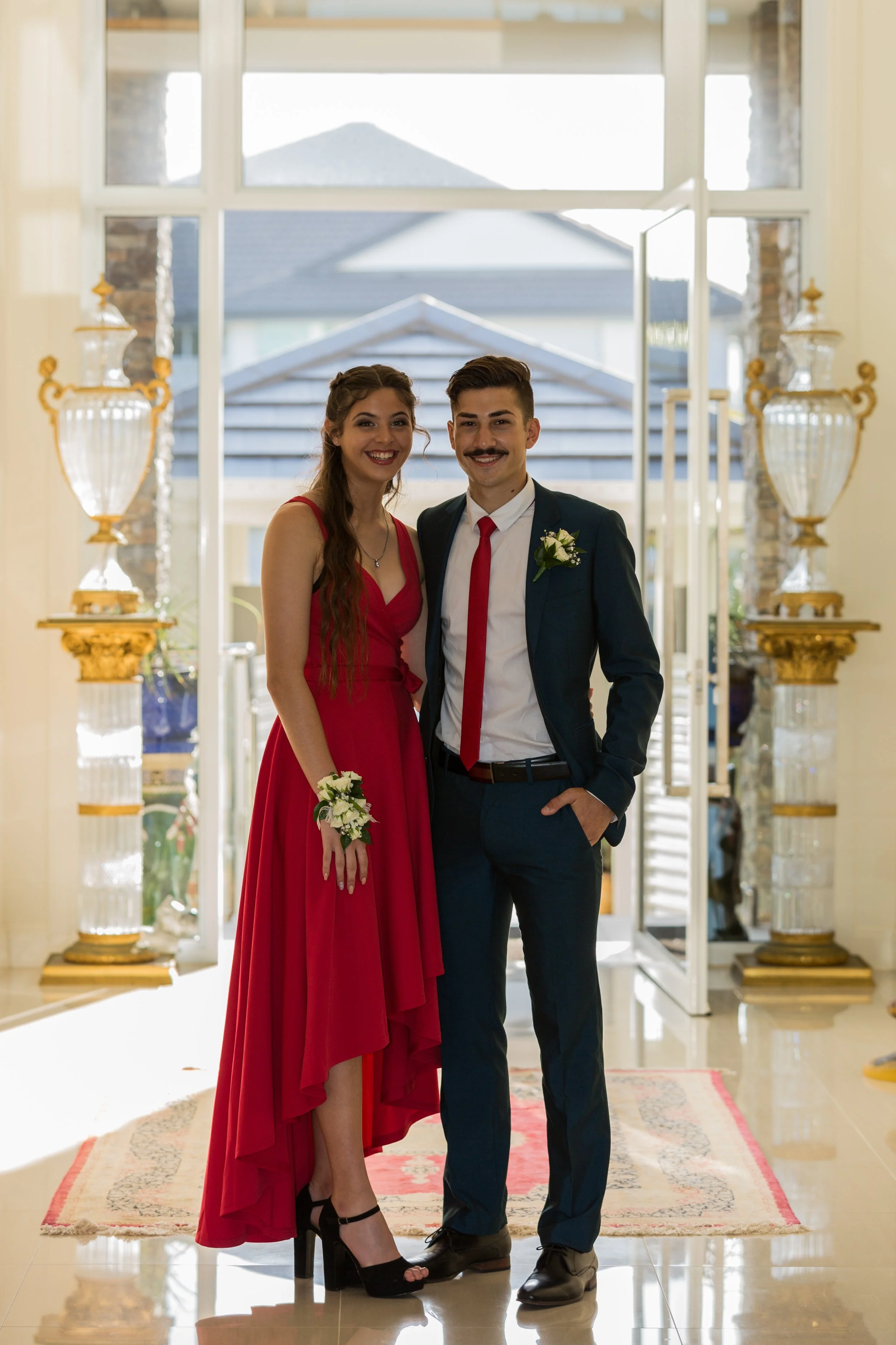 Formal school couple stand inside a mansion hallway all dressed up.