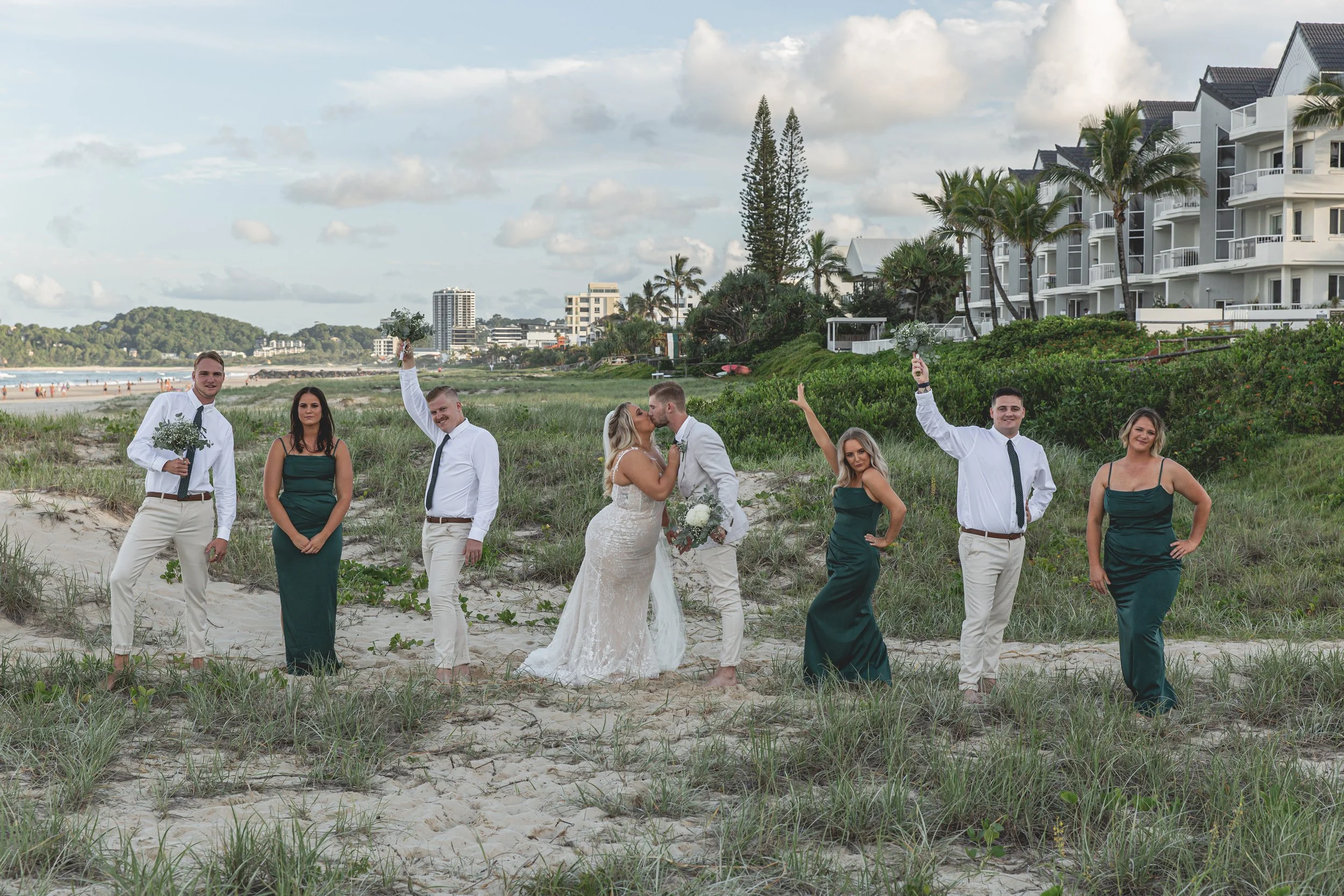 Silly bridal party on Gold Coast Beach with newly married couple sharing a kiss. 