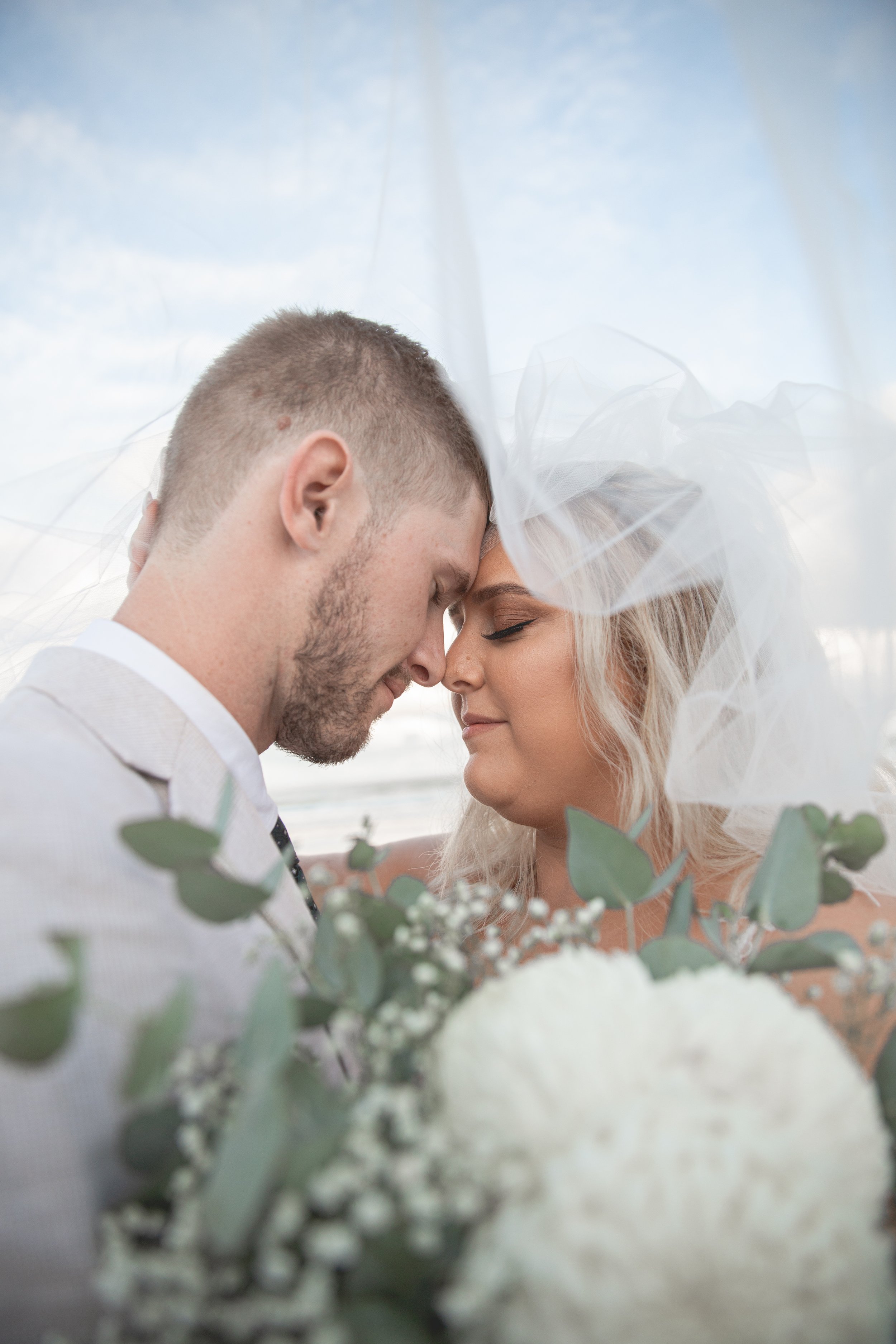 Couple under veil with a bouquet of flowers on Gold Coast beach.