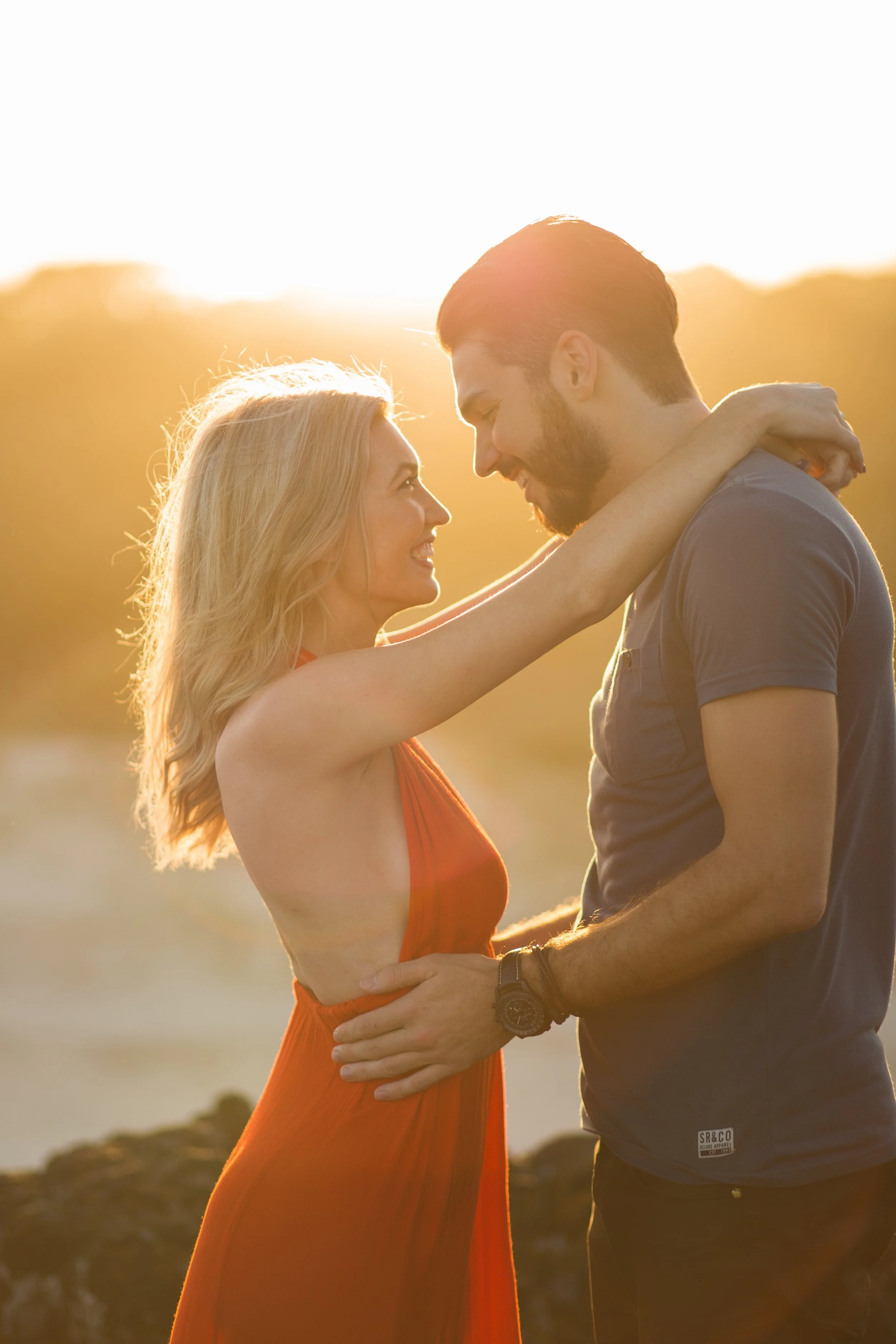 Couple embracing each other with a stunning golden sunset behind them at Fingal Lighthouse Lookout. 