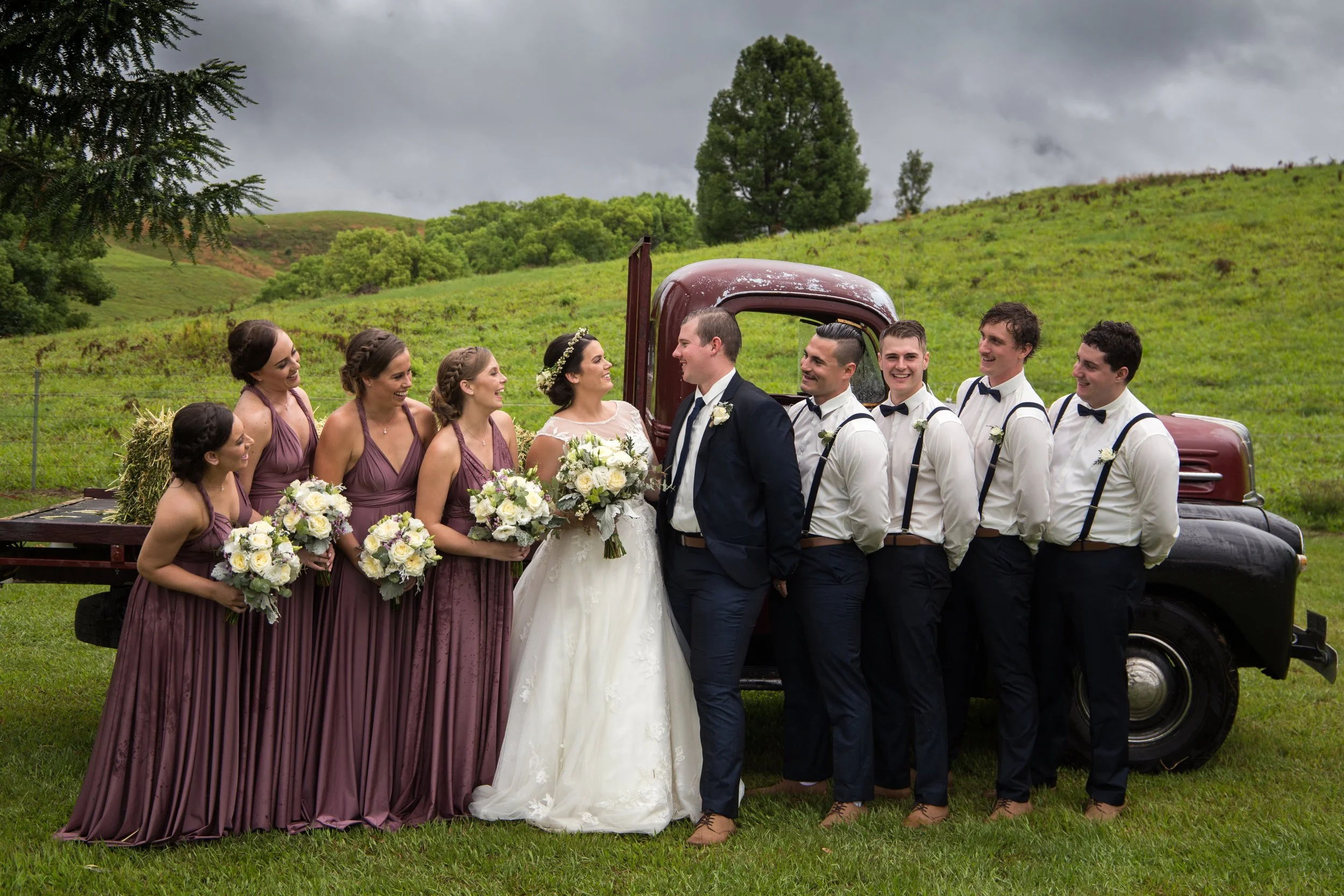 Wedding couple admire each other with the bridal party surrounding them by the farm truck. 