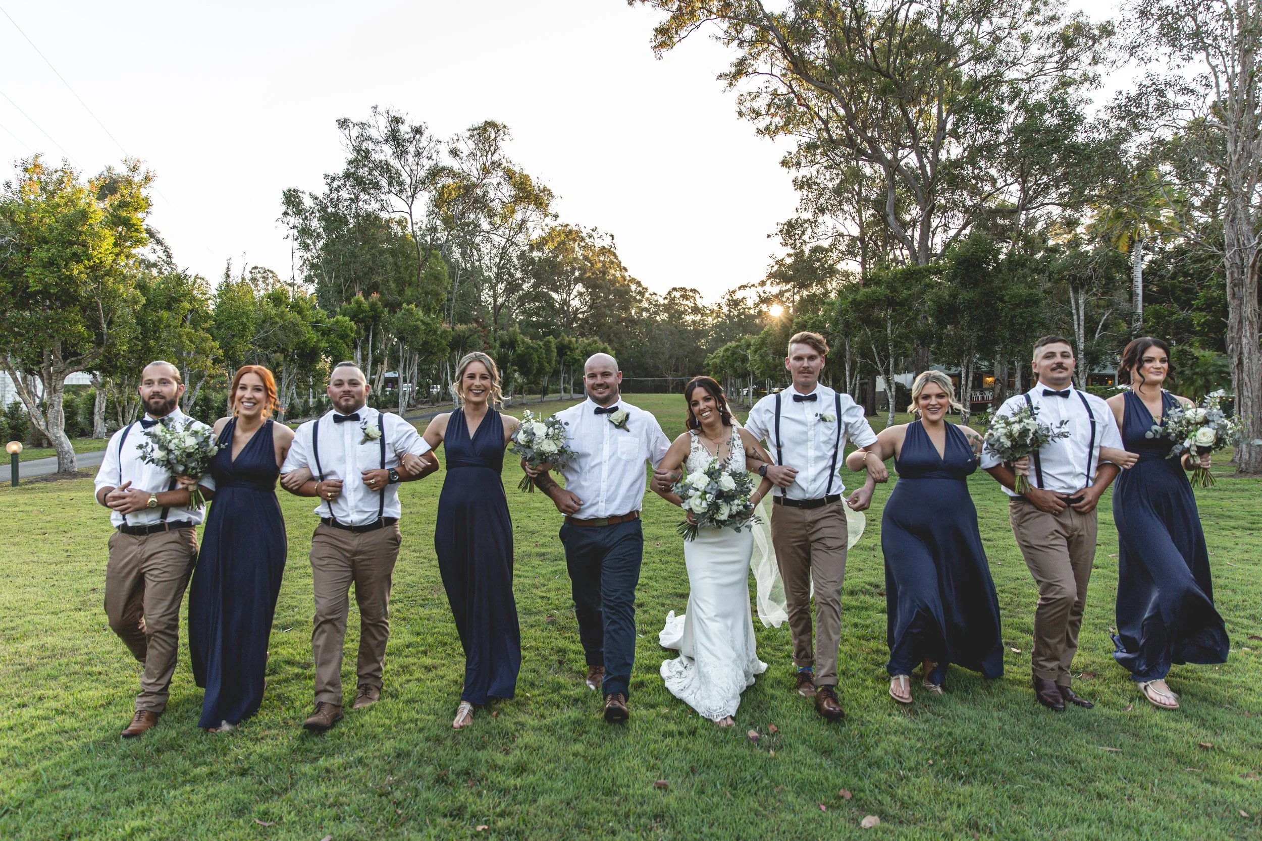 Bridal party linking arms and laughing at Coolabah Downs Private Estate during stunning sunset. 