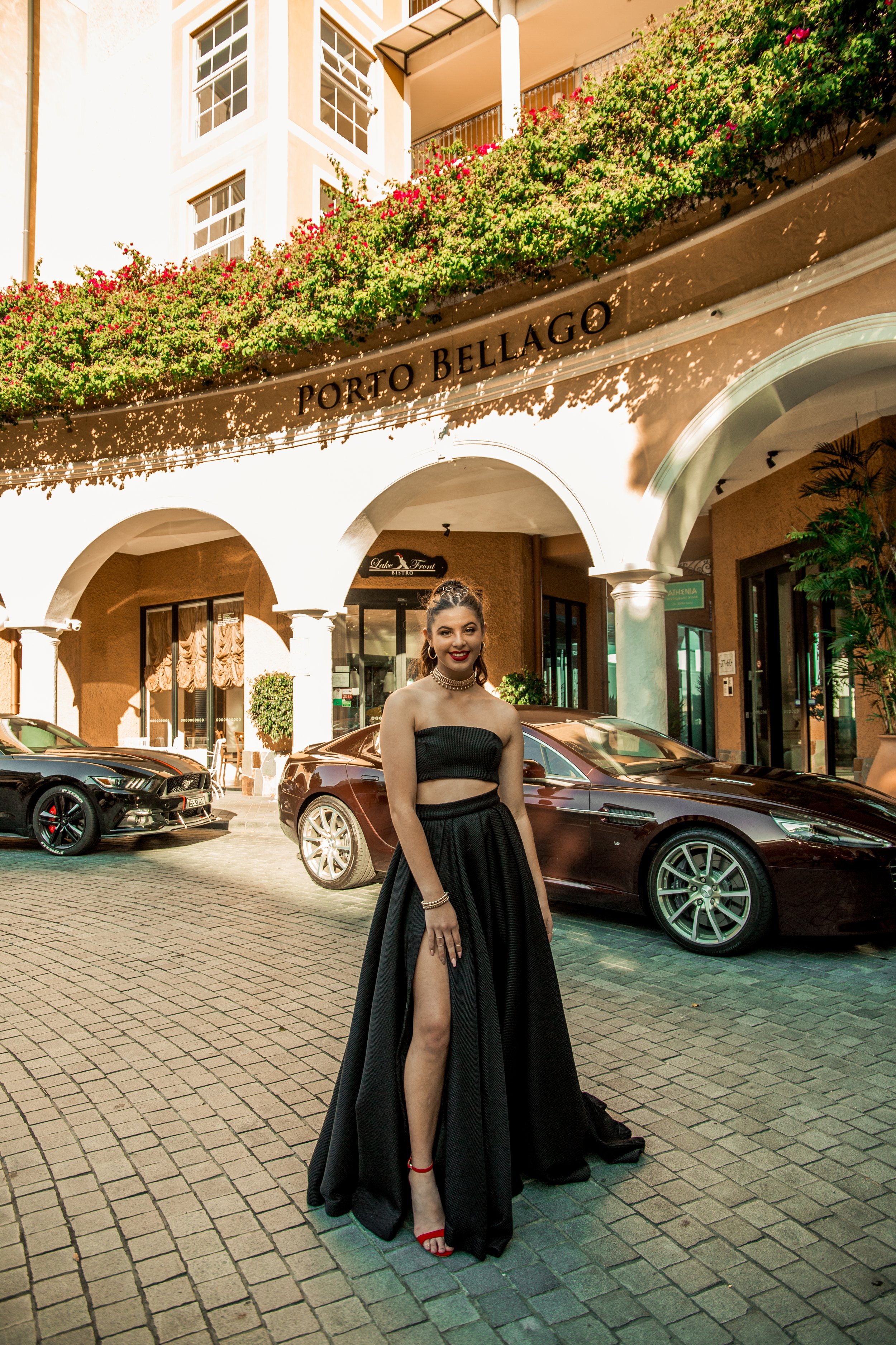 Female in black dress modelling in front expensive cars during golden sunset at Emerald Lakes for stunning portrait.