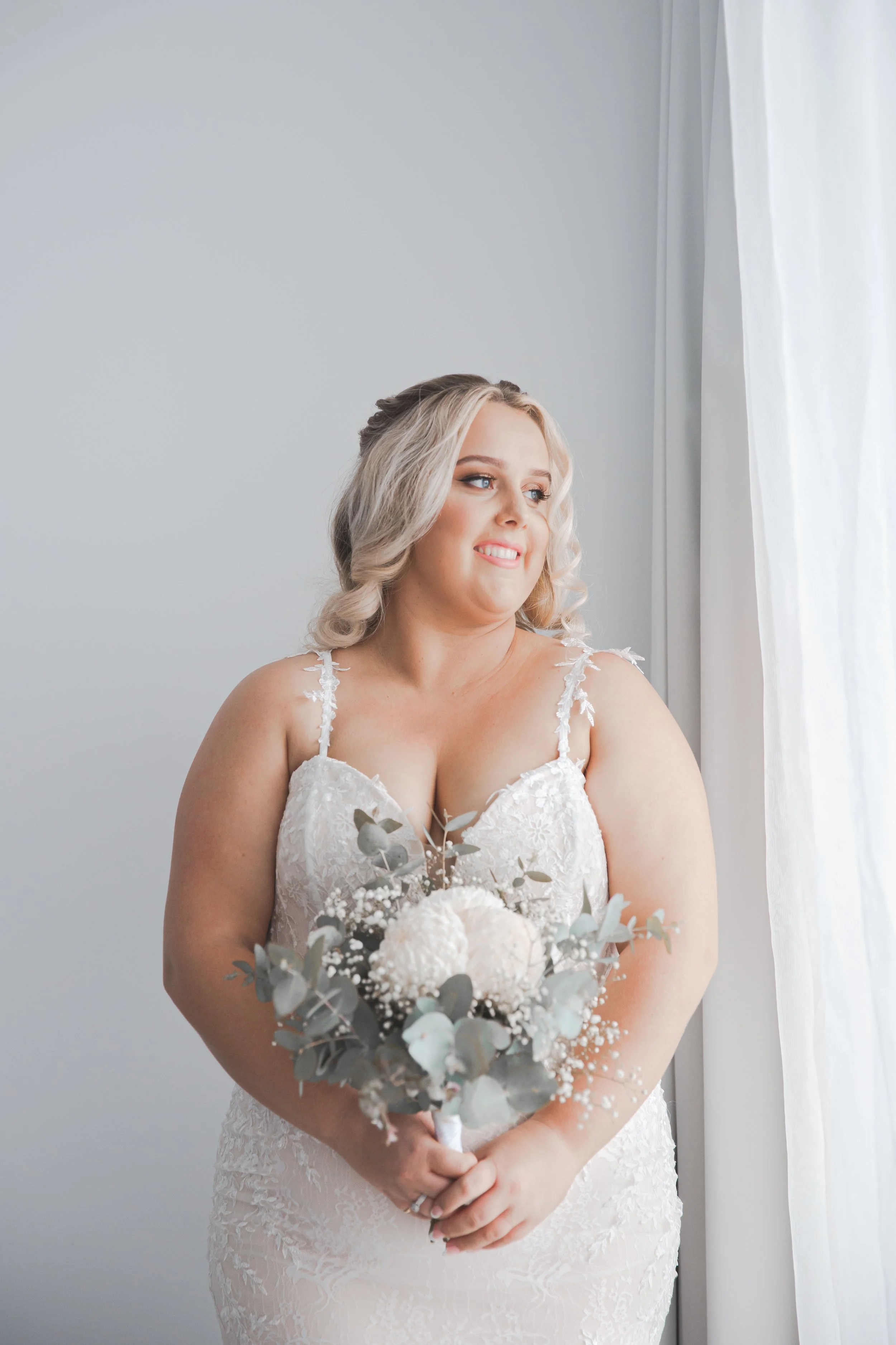 Woman in wedding dress holding bouquet looking out window at Peppers Broadbeach.