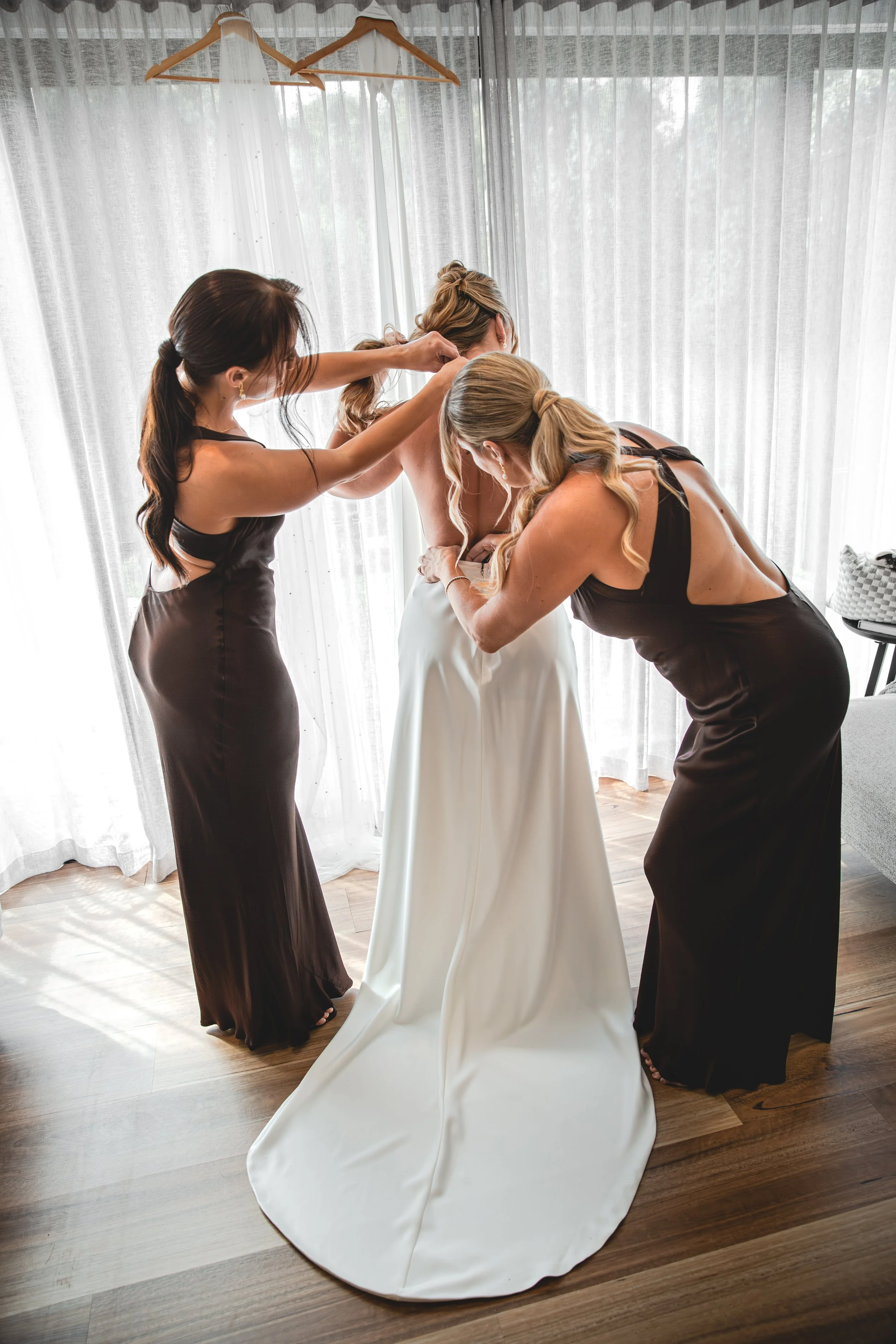 Bride getting helped into wedding dress by bridesmaids at Selah Valley Estate Creekside Lodge.