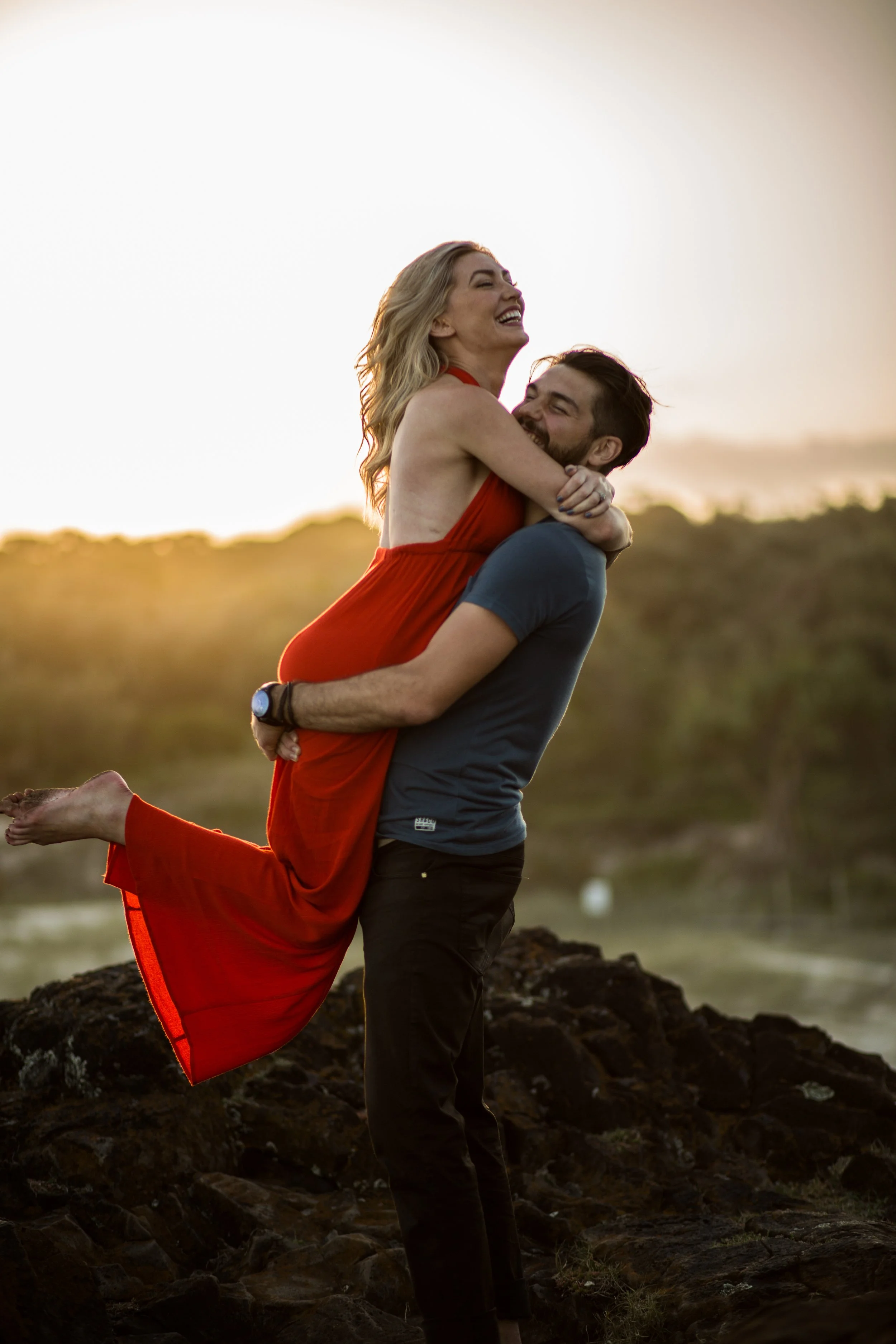 Male picks up female partner for a couples portrait with natural golden light at Fingal Lighthouse Lookout. 