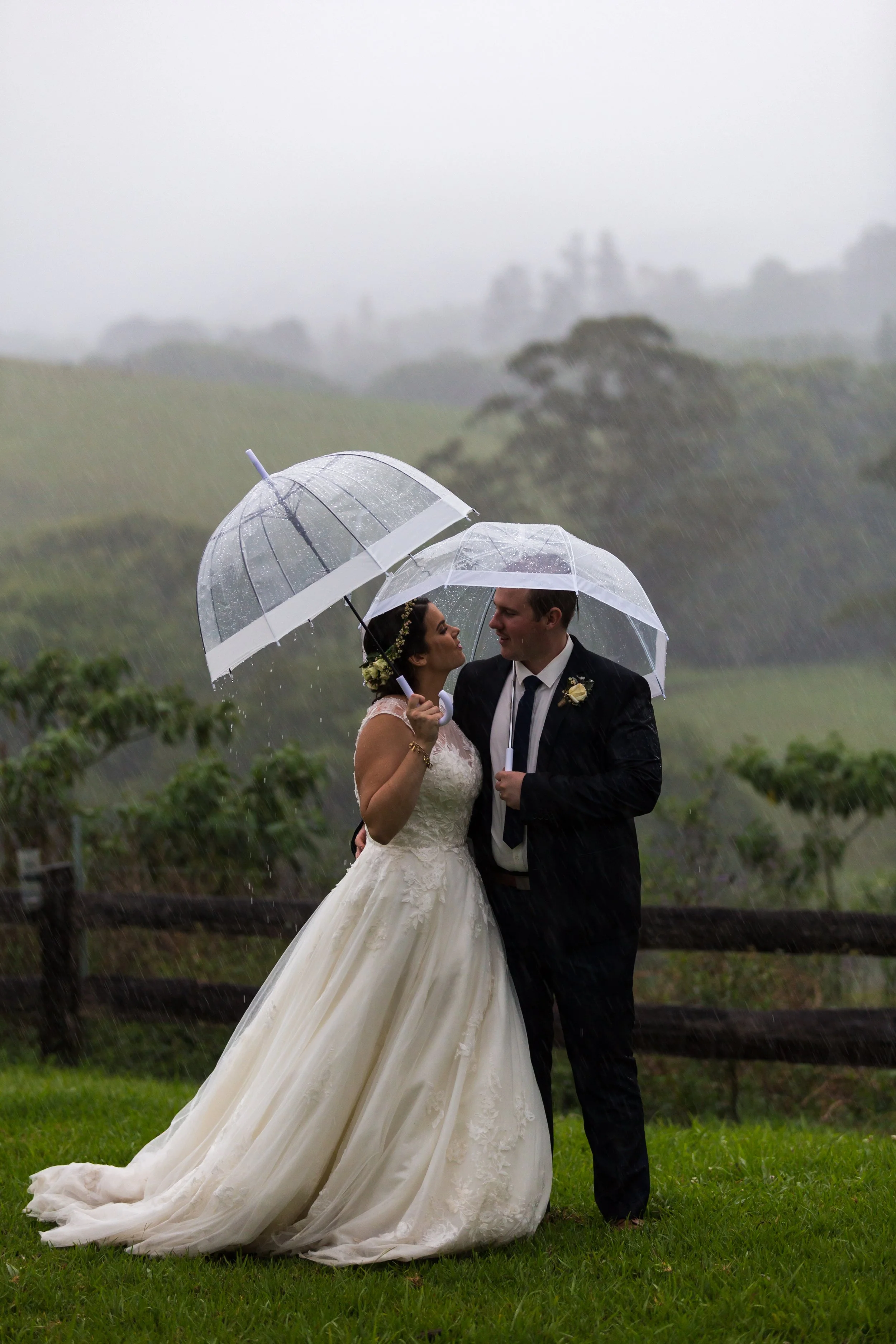 Wedding couple under clear umbrellas during heavy rain fall. 