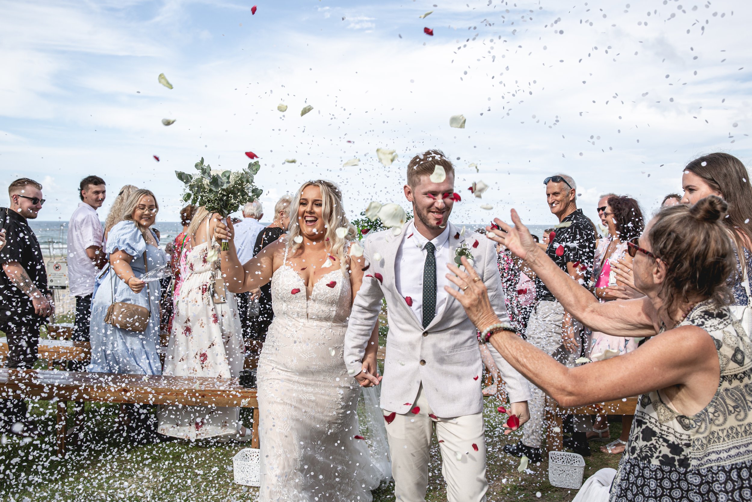 Newly wed couple walk down isle with rose petals getting thrown at Gold Coast beach wedding.