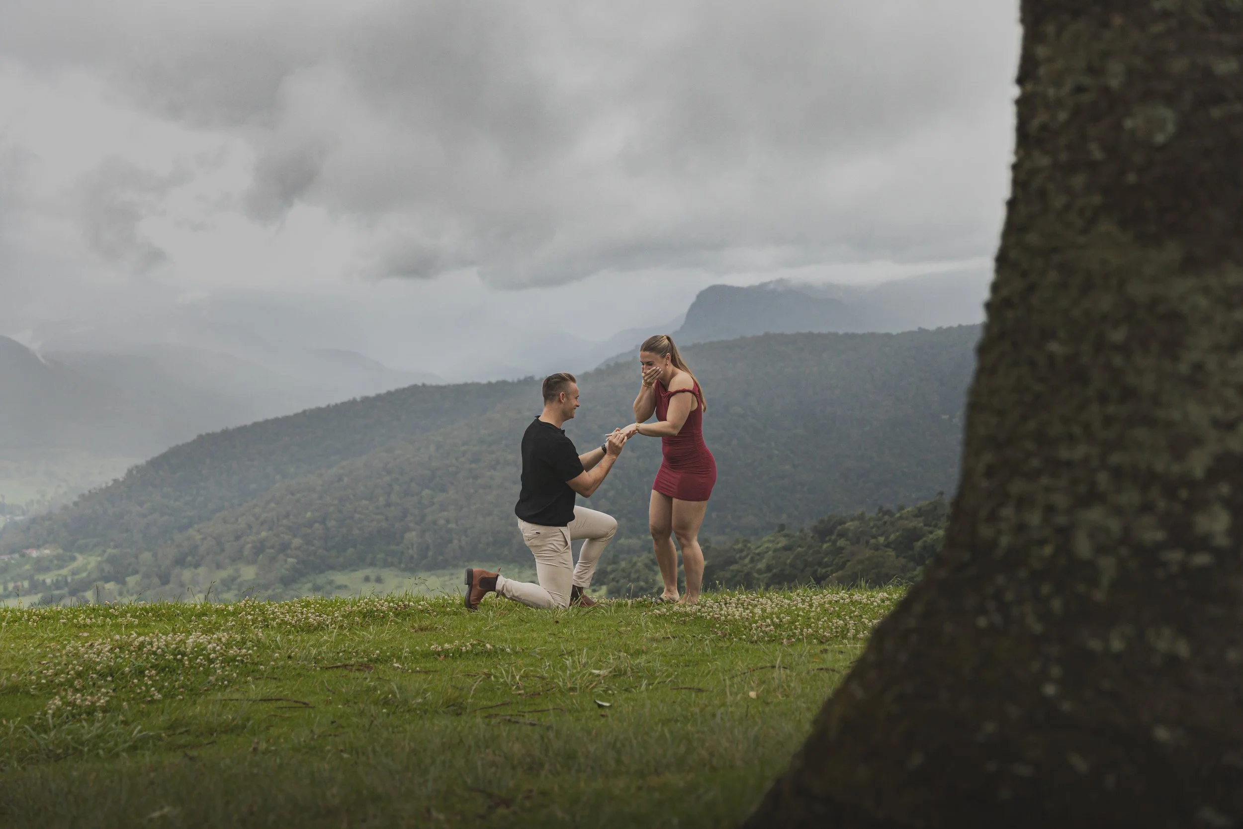 Male gets on one knee and proposes to female during a cloudy afternoon at a Beechmont lookout.  