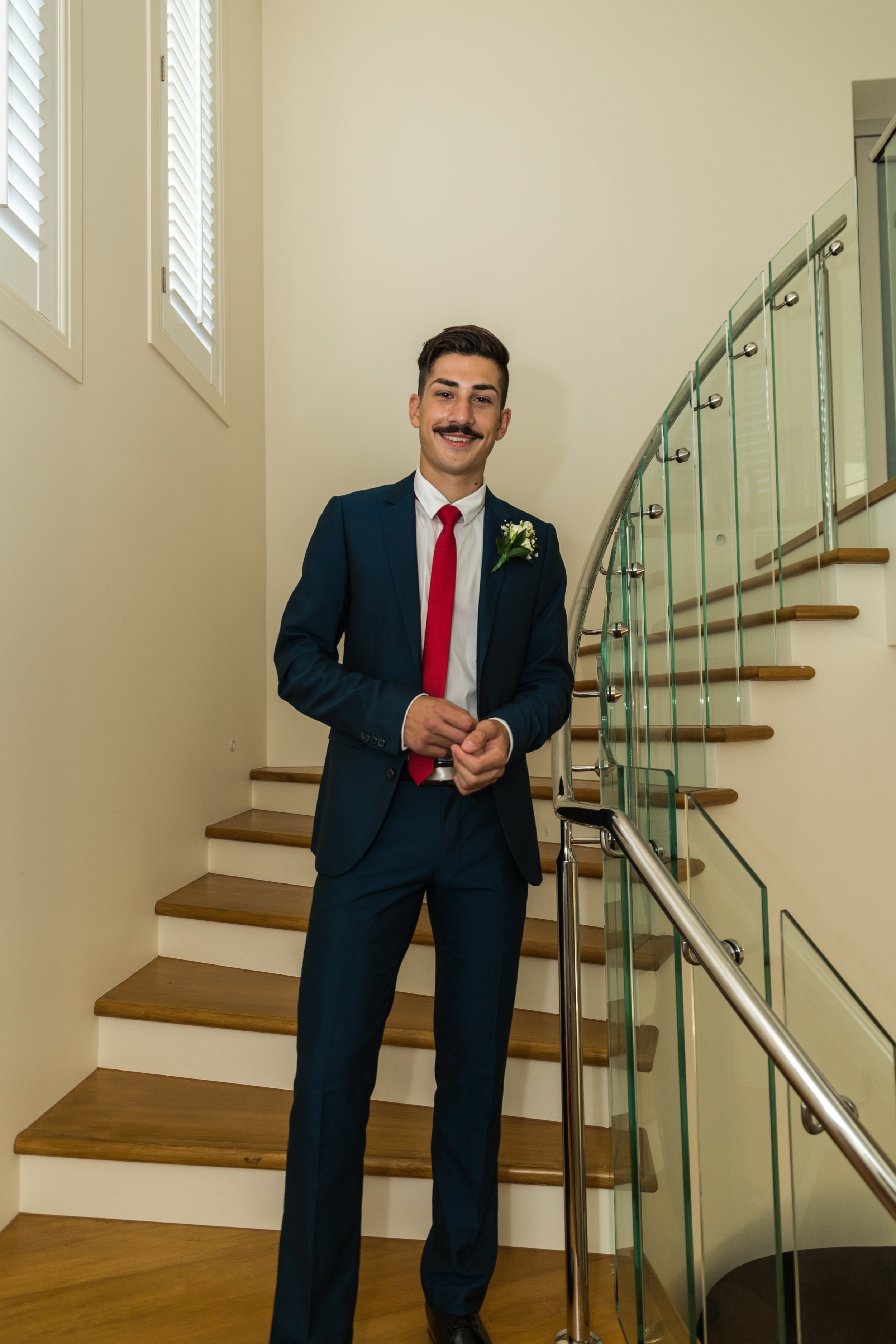 Formal student in suit and tie stands on stairs inside mansion with natural lighting.