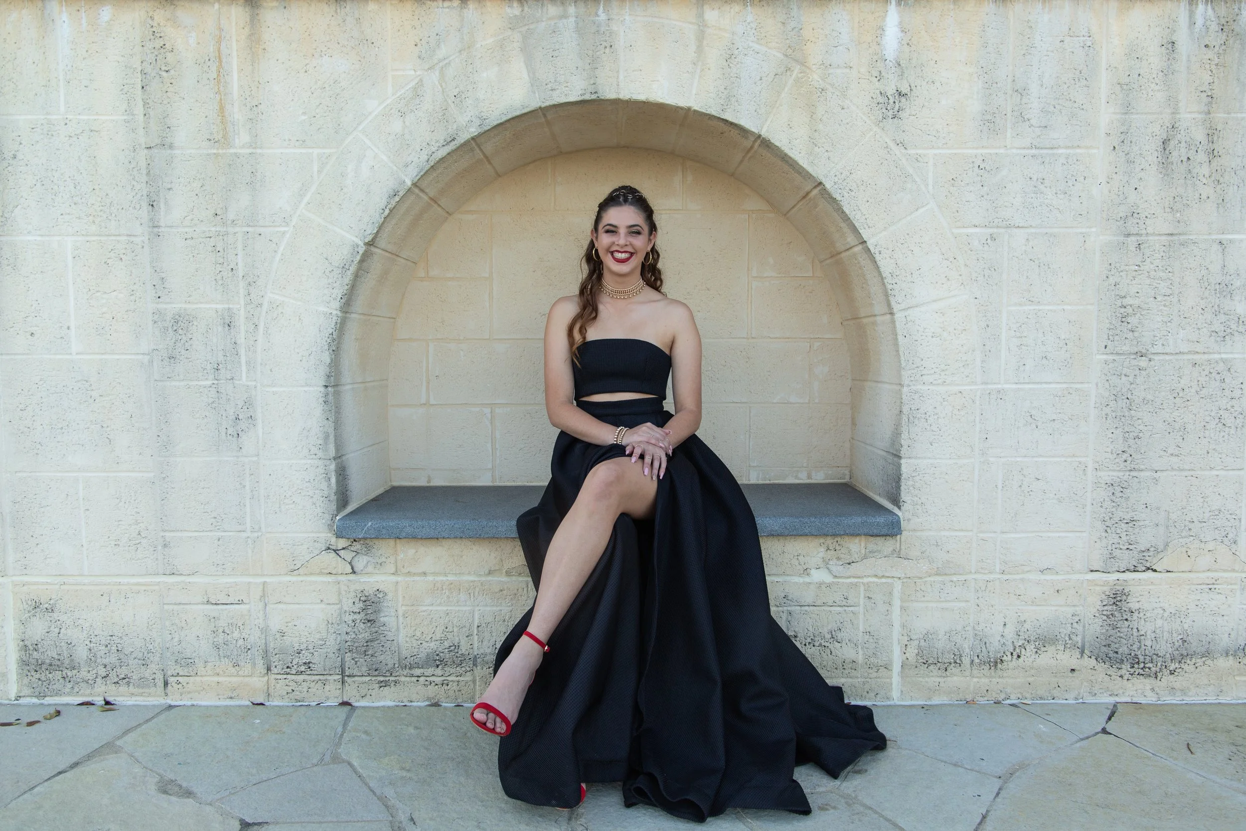 Formal student in black dress sitting on bench in massive concrete arch at Emerald Lakes.