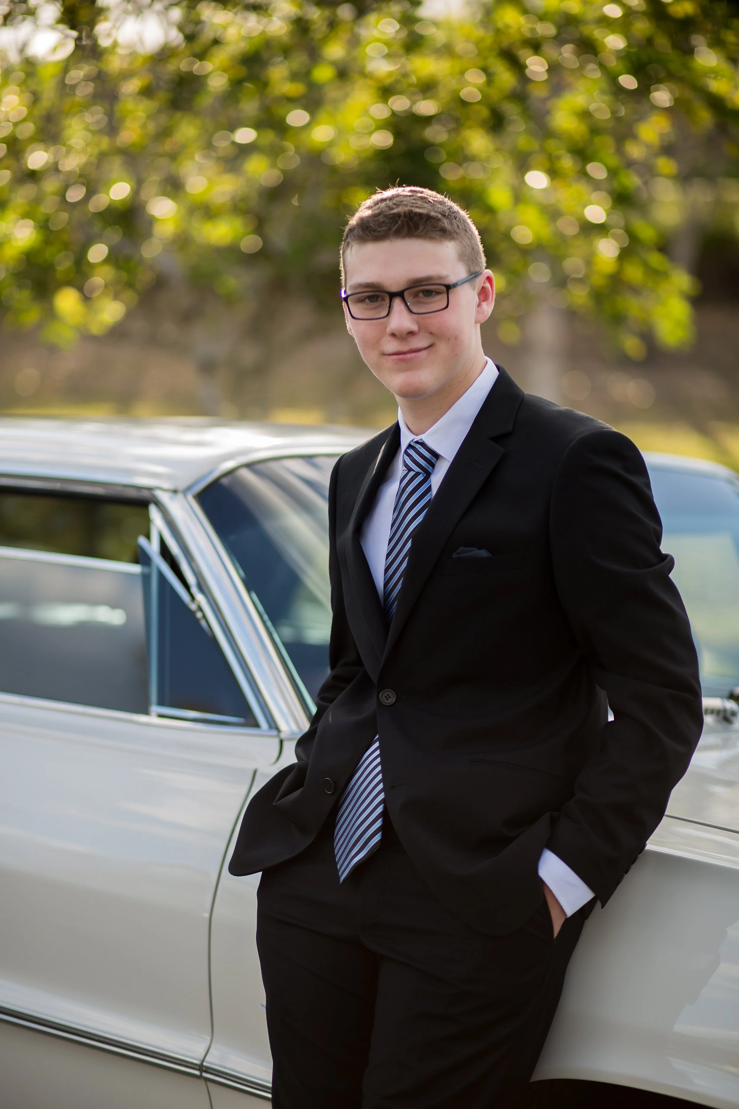 Formal student stands with vintage car with golden sunset.