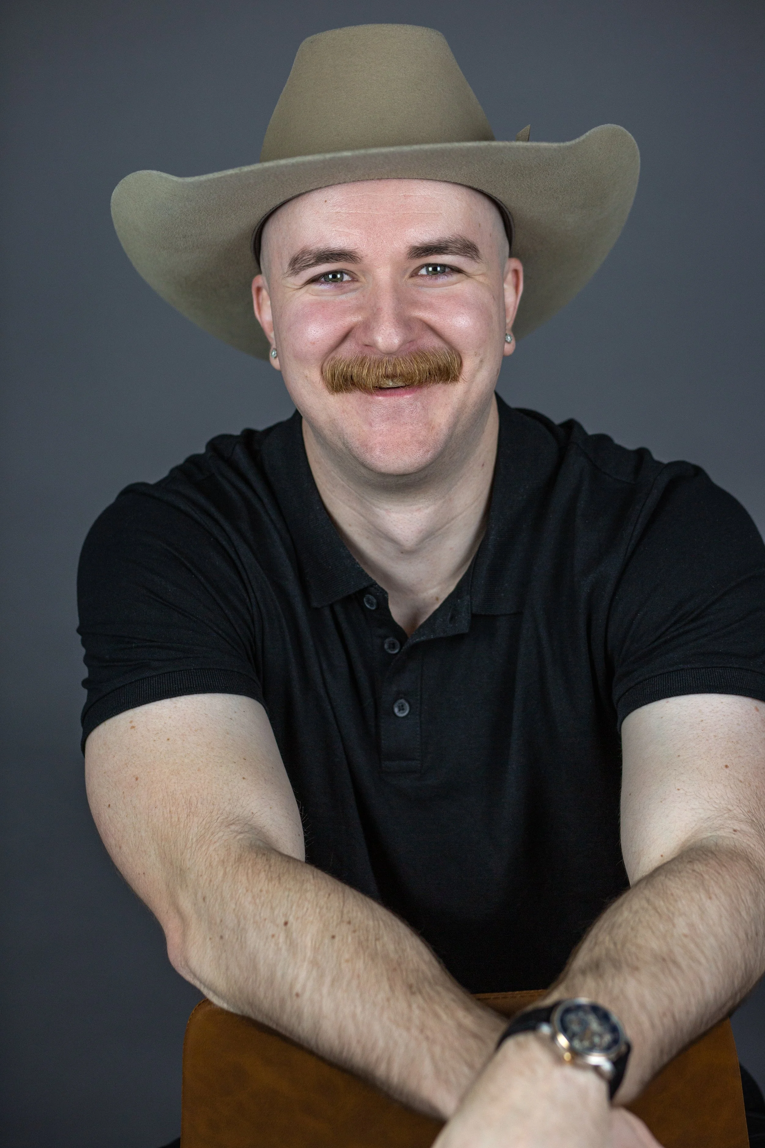 Owner of Furlonger Images poses in studio while wearing a cowboy hat and laughing.
