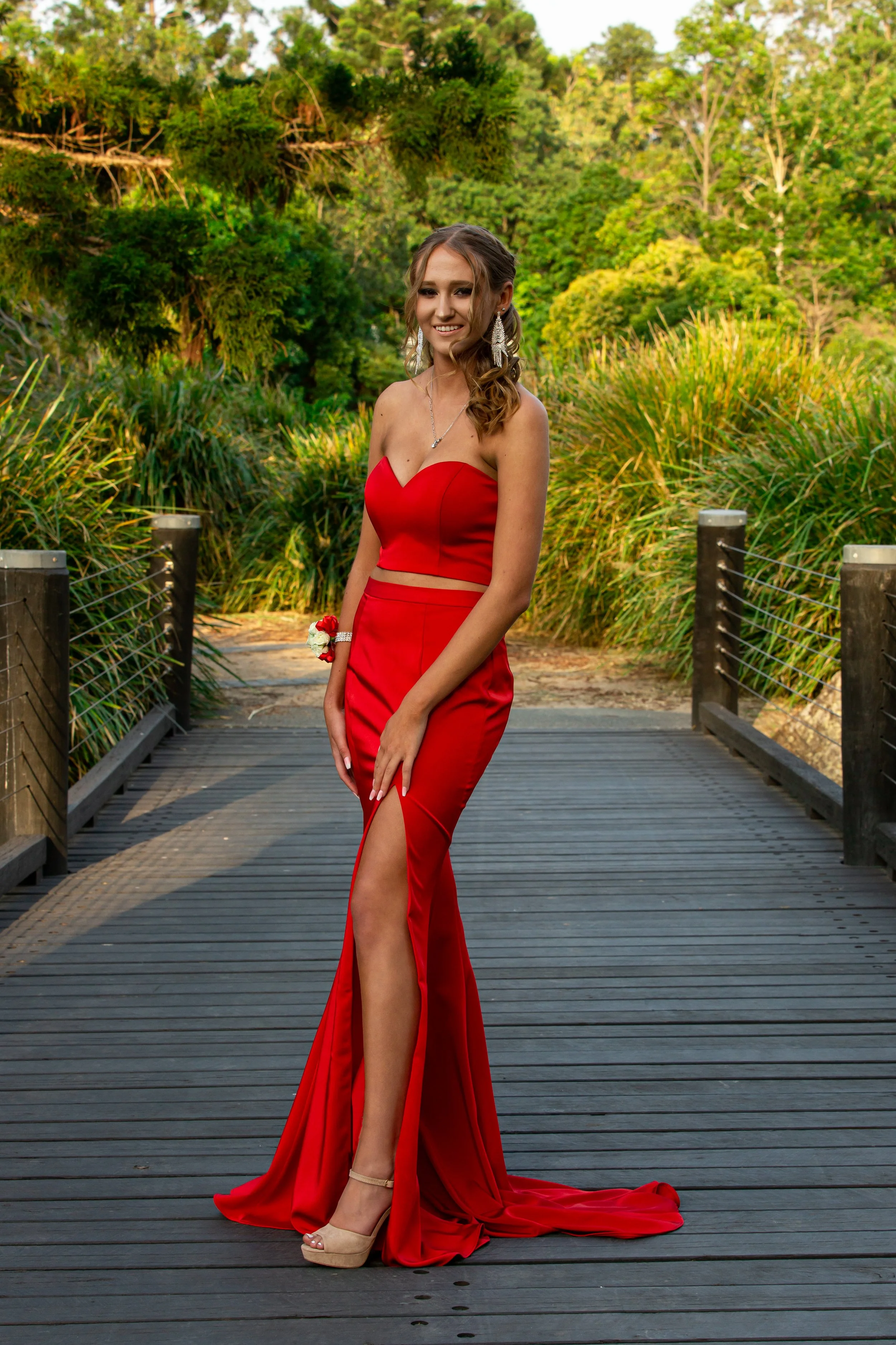 Student going to school formal stands in long red dress on bridge during golden sunset at Benowa Botanical Gardens.