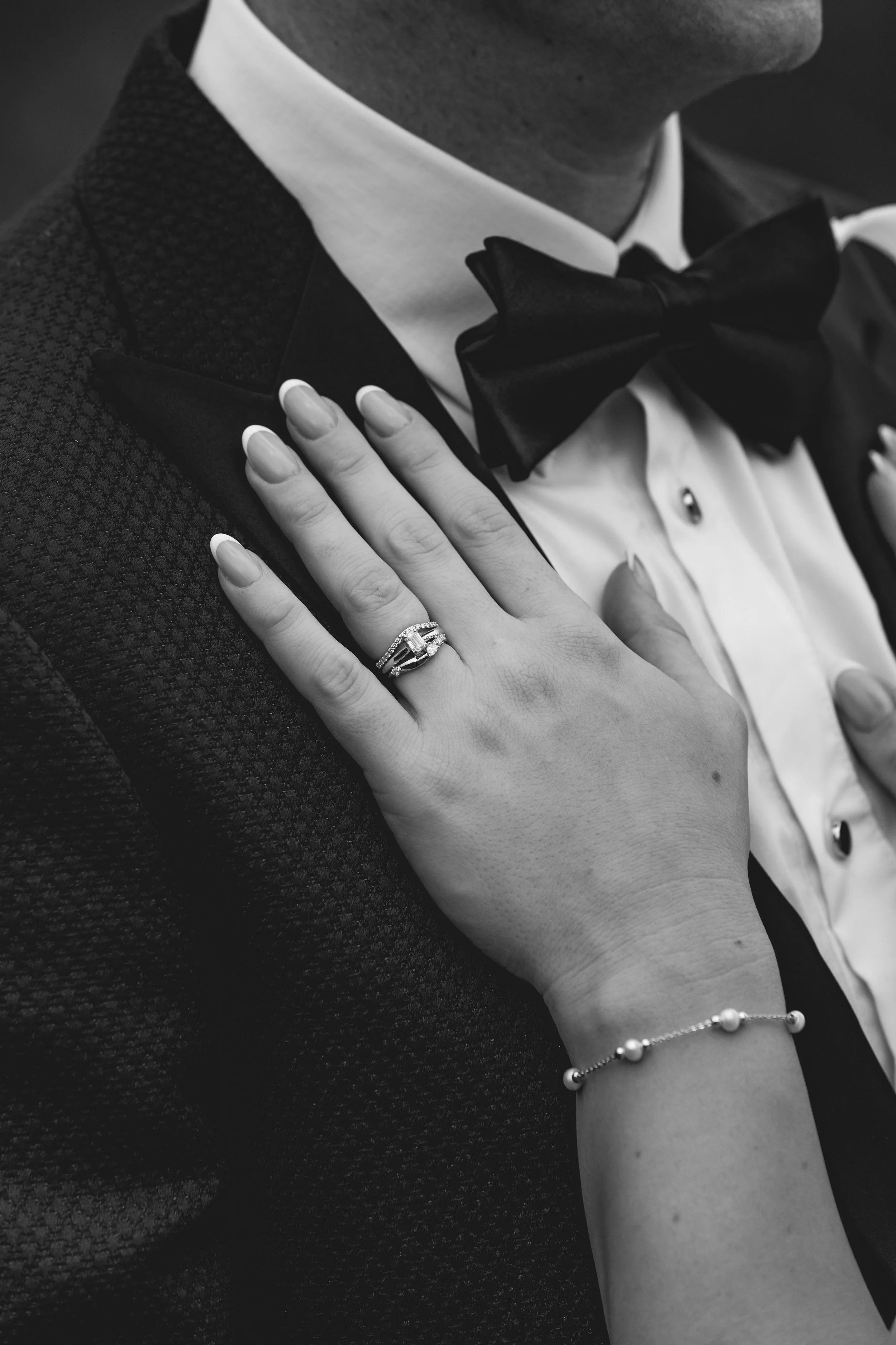 close up of brides hands on grooms chest showing rings in detail.