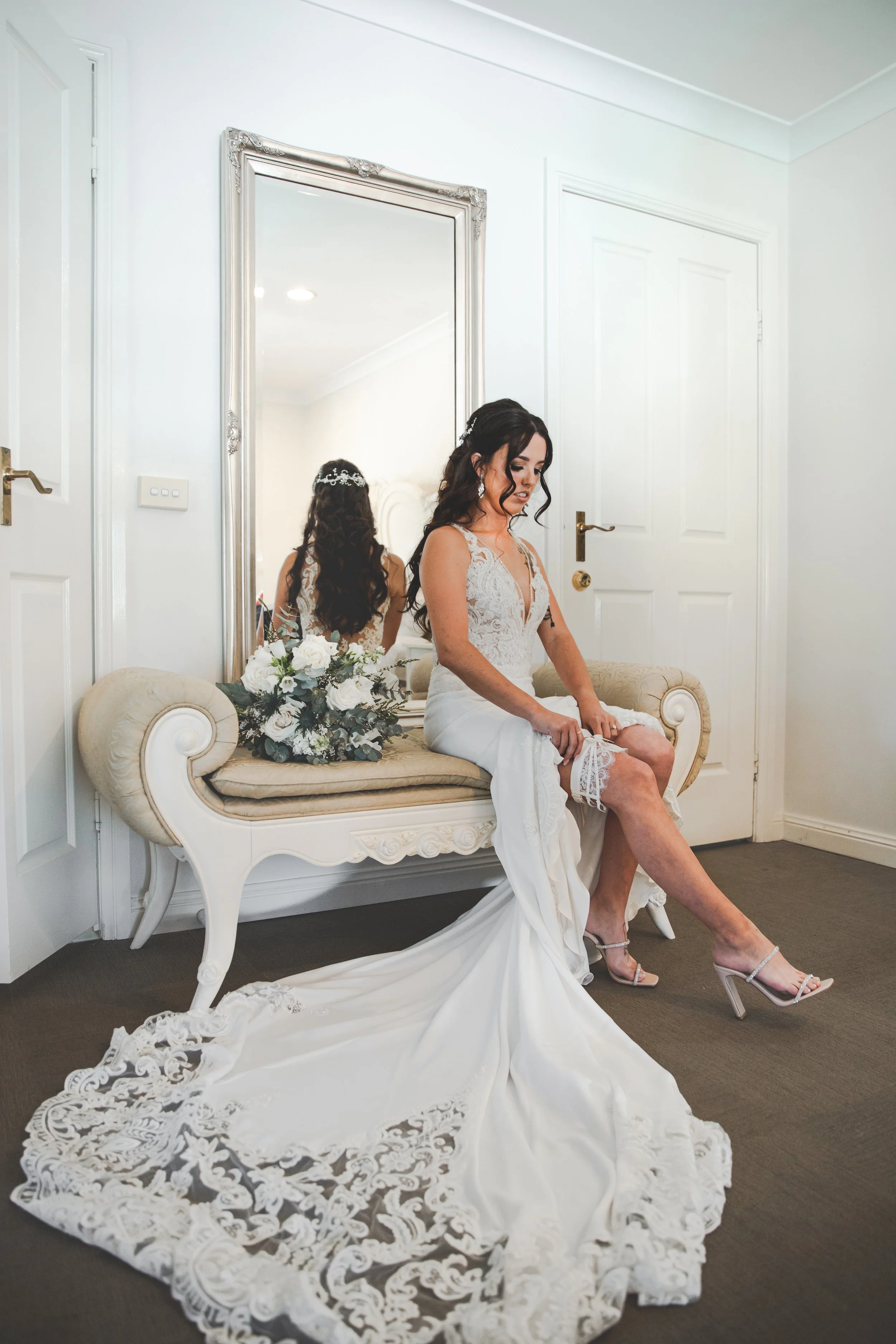 Woman in wedding dress adjusting the garter while sitting on antique lounge at Coolabah Downs Private Estate. 