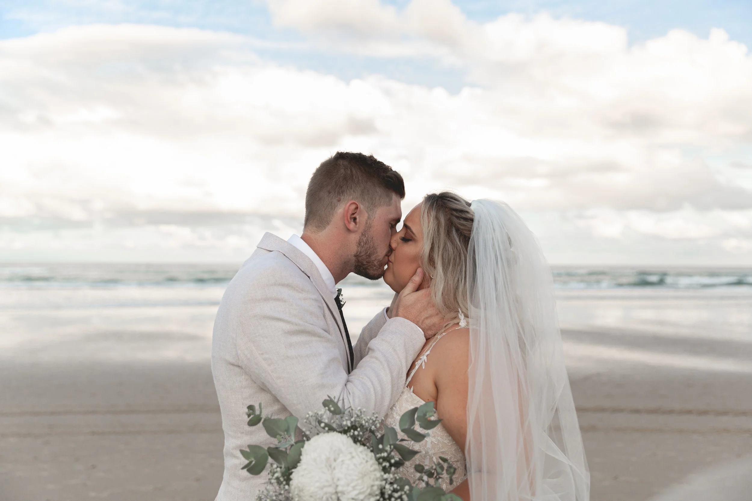 Couple getting married on a Gold Coast sharing a kiss by the waves on the beach.