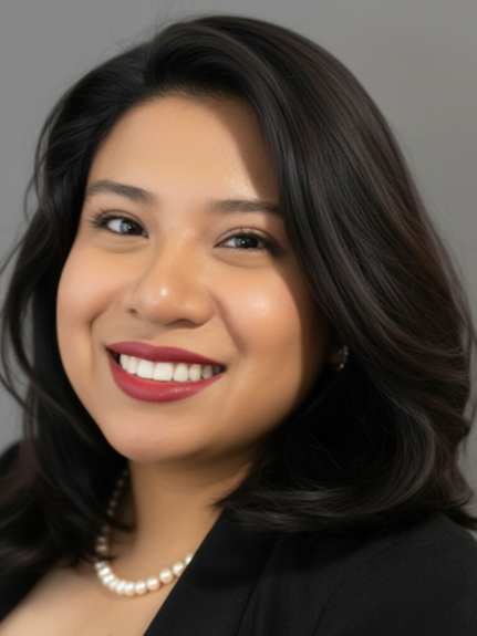 Close-up of a smiling woman with dark hair, red lipstick, pearl necklace, and a black blazer against a gray background.