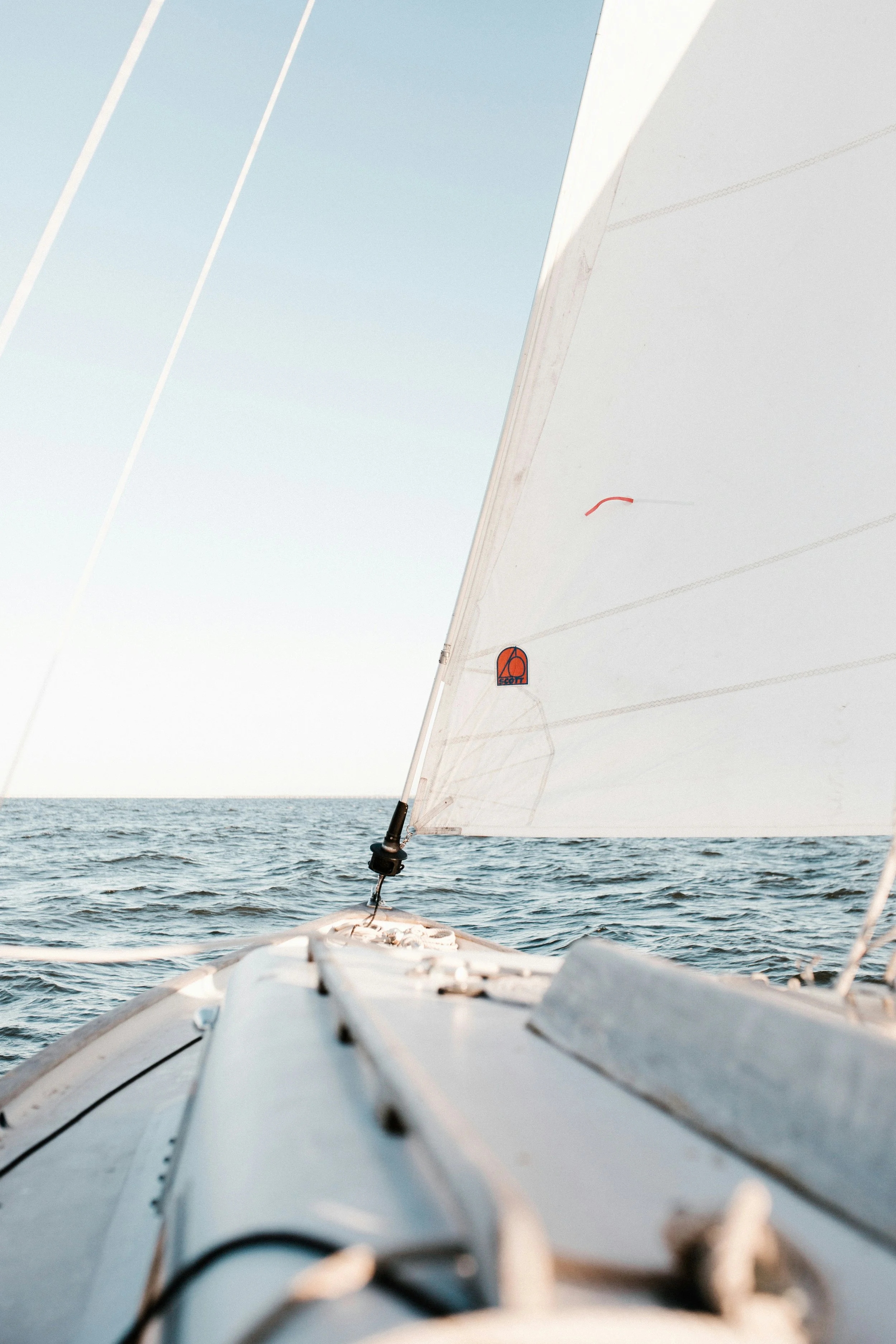 View from the bow of a sailboat on open water with a partially visible sail.