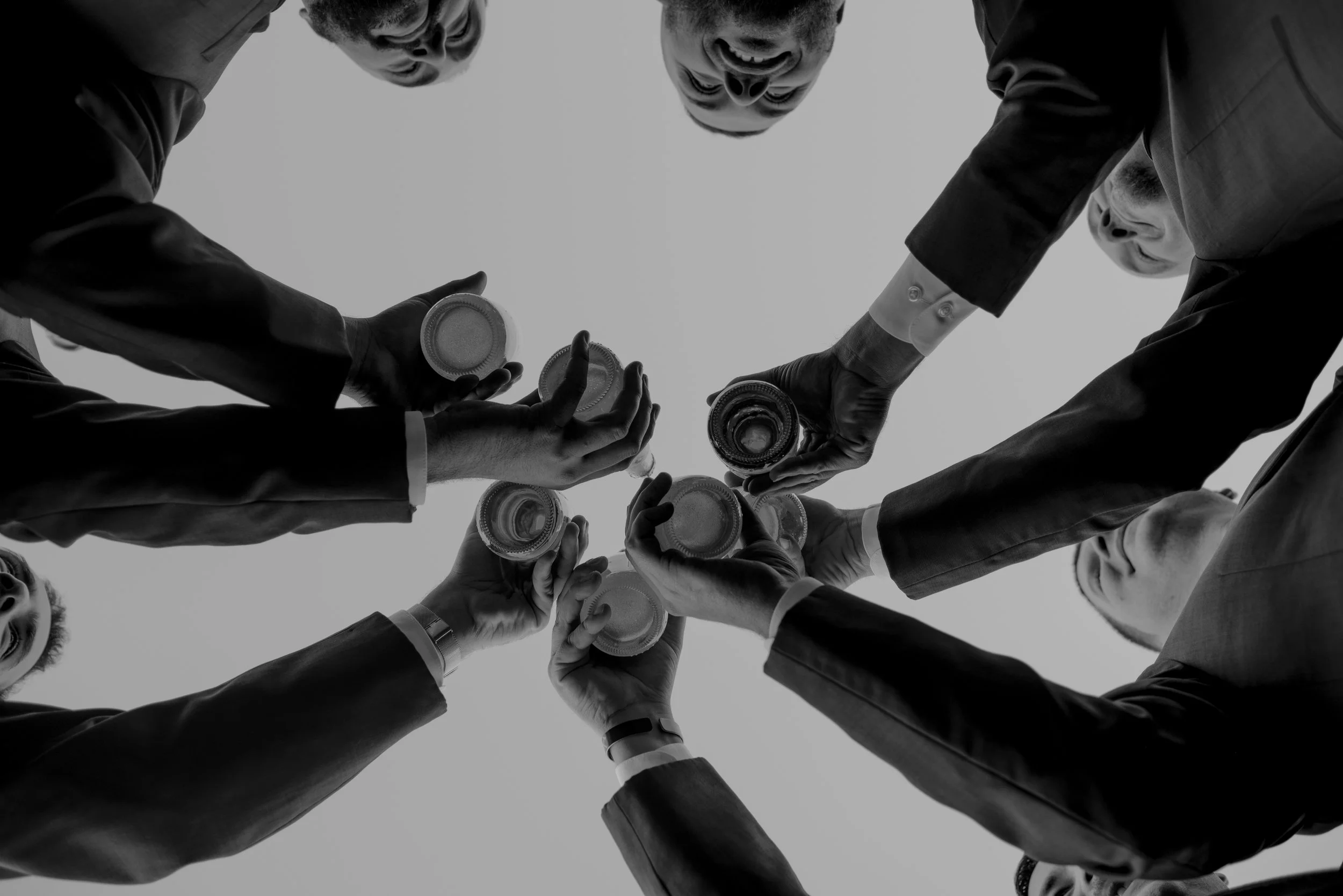 Multiple people in business suits forming a circle with their arms extended downward and holding empty glass jars or containers, viewed from below against a plain background.