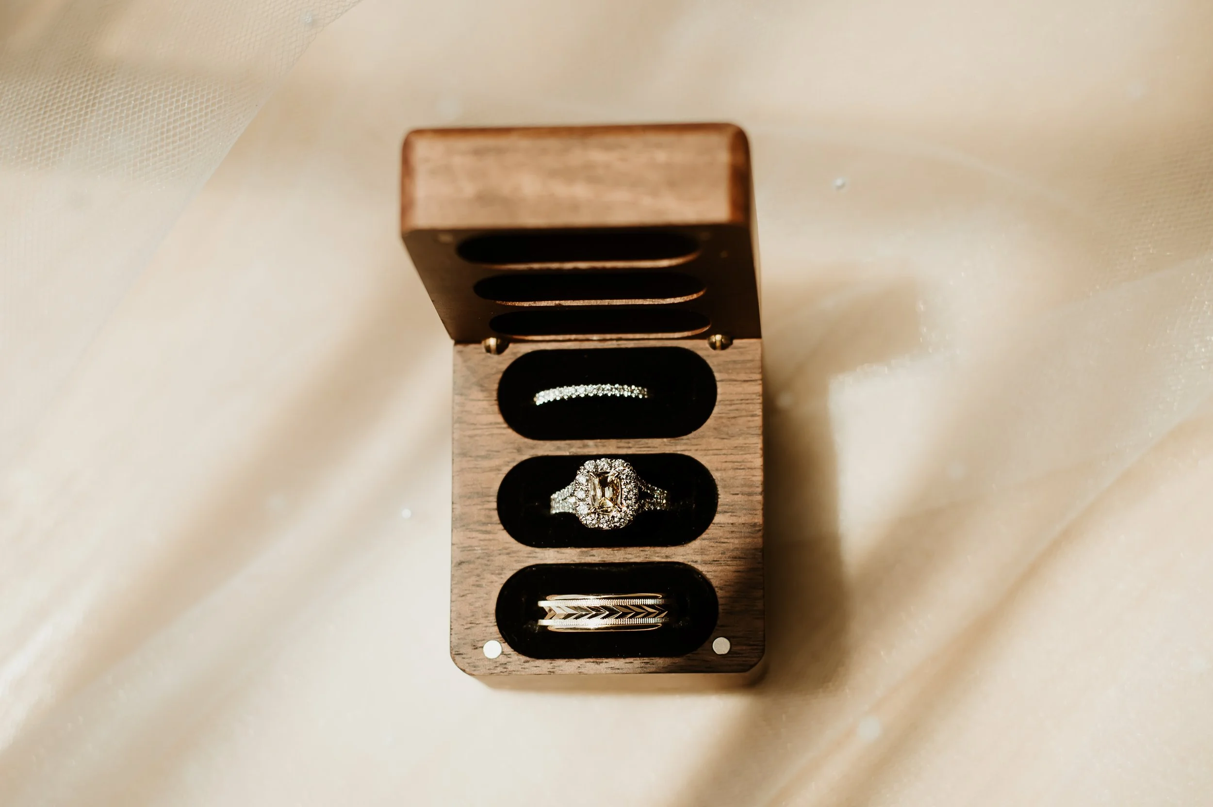 Close-up of a wooden jewelry display stand with a diamond ring on it, set against a soft, white fabric background.