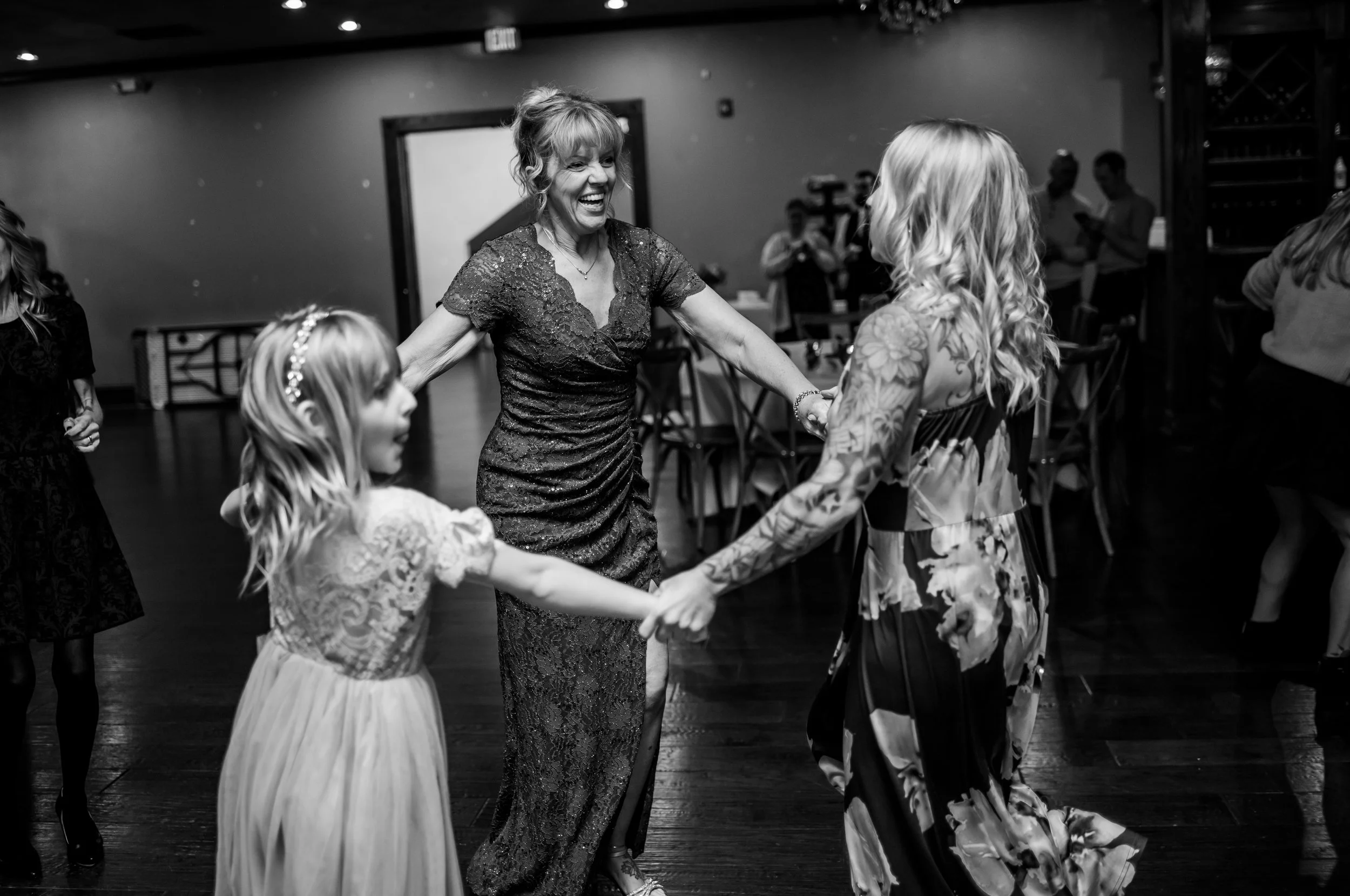 Women and girls dancing in a circle at an indoor event, smiling and holding hands.