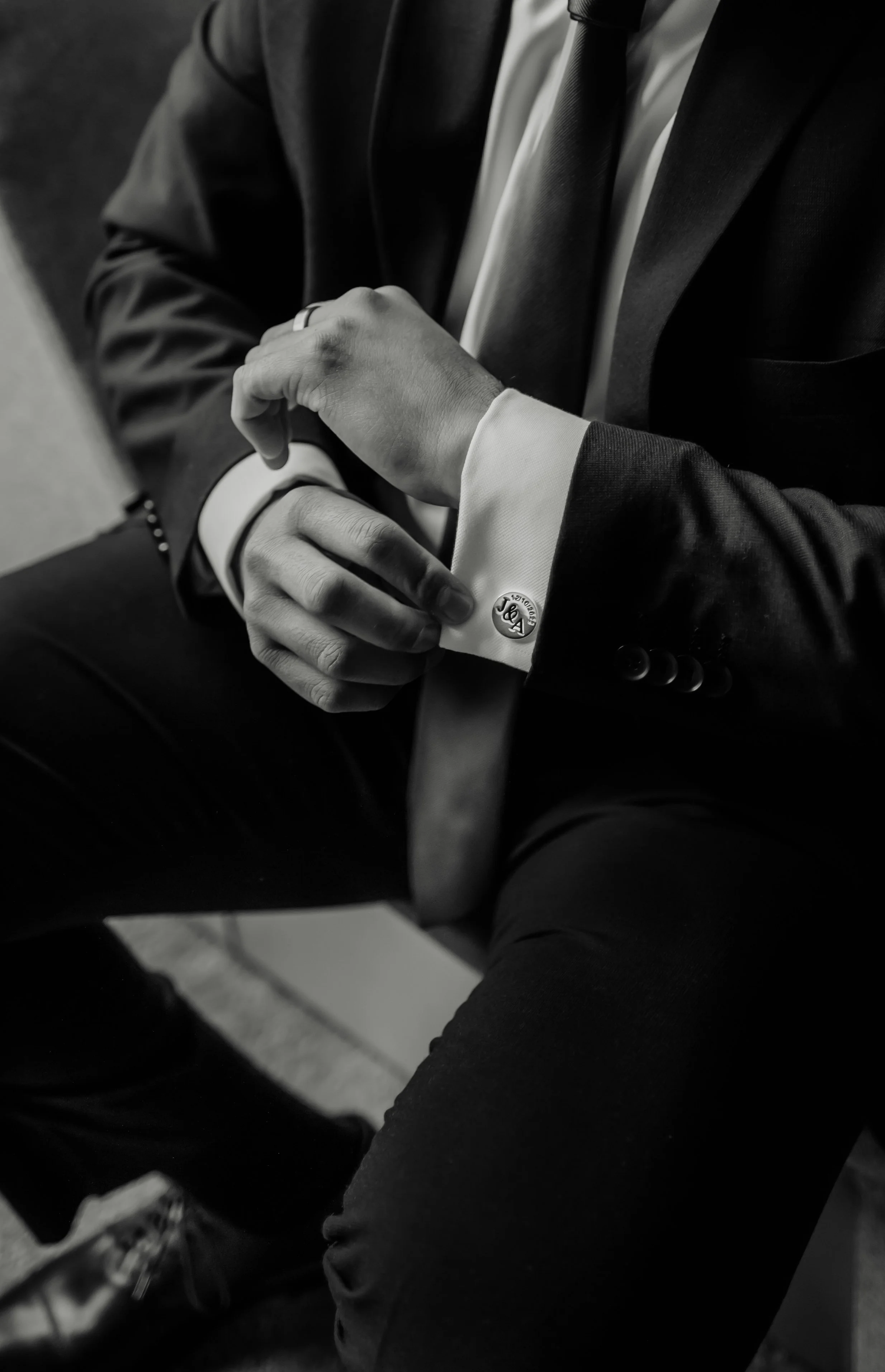 Close-up of a man wearing a suit, adjusting his cufflink on his sleeve, in black and white.
