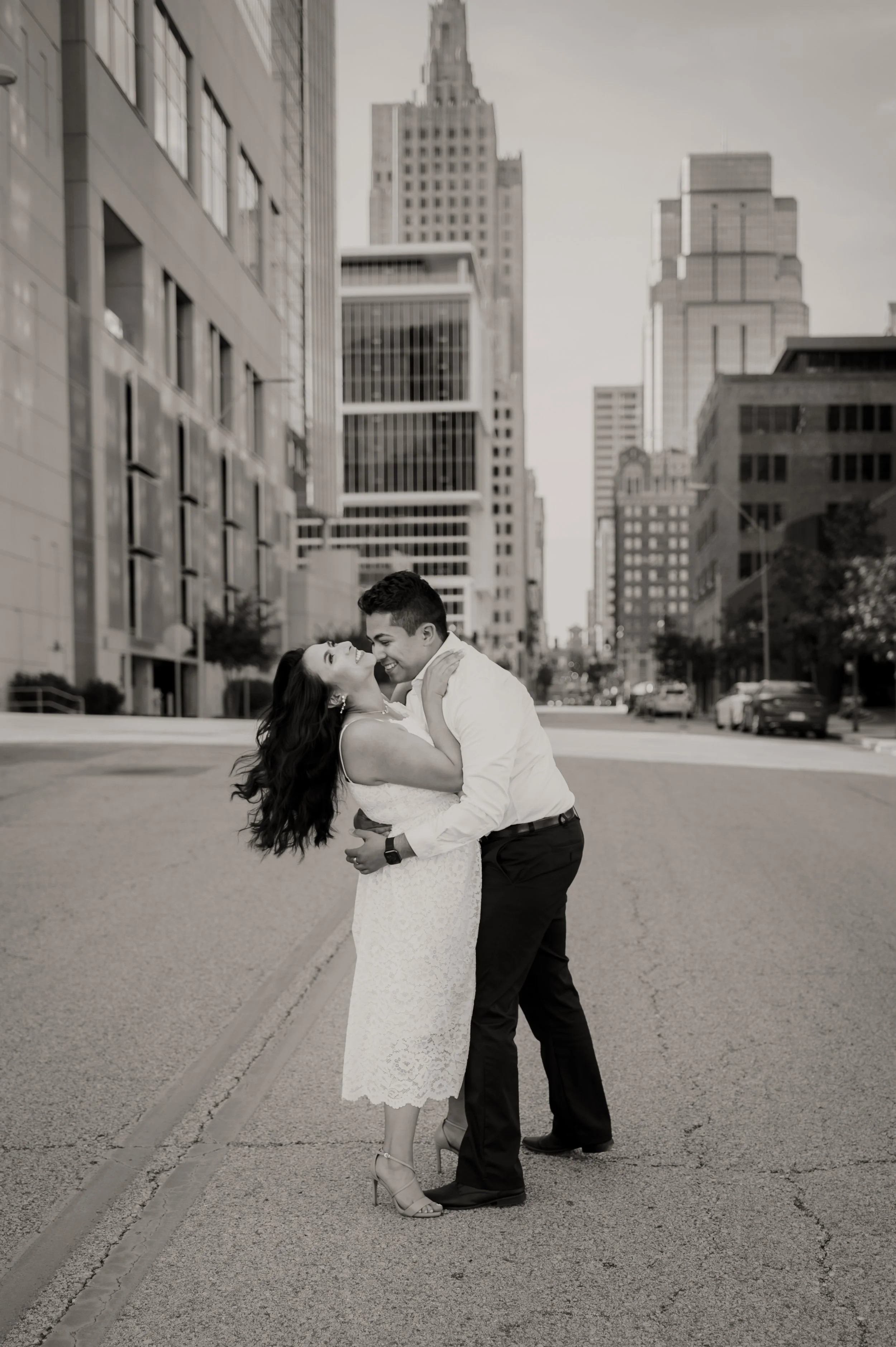 A joyful couple dancing in the middle of a city street with tall buildings in the background, captured in black and white.
