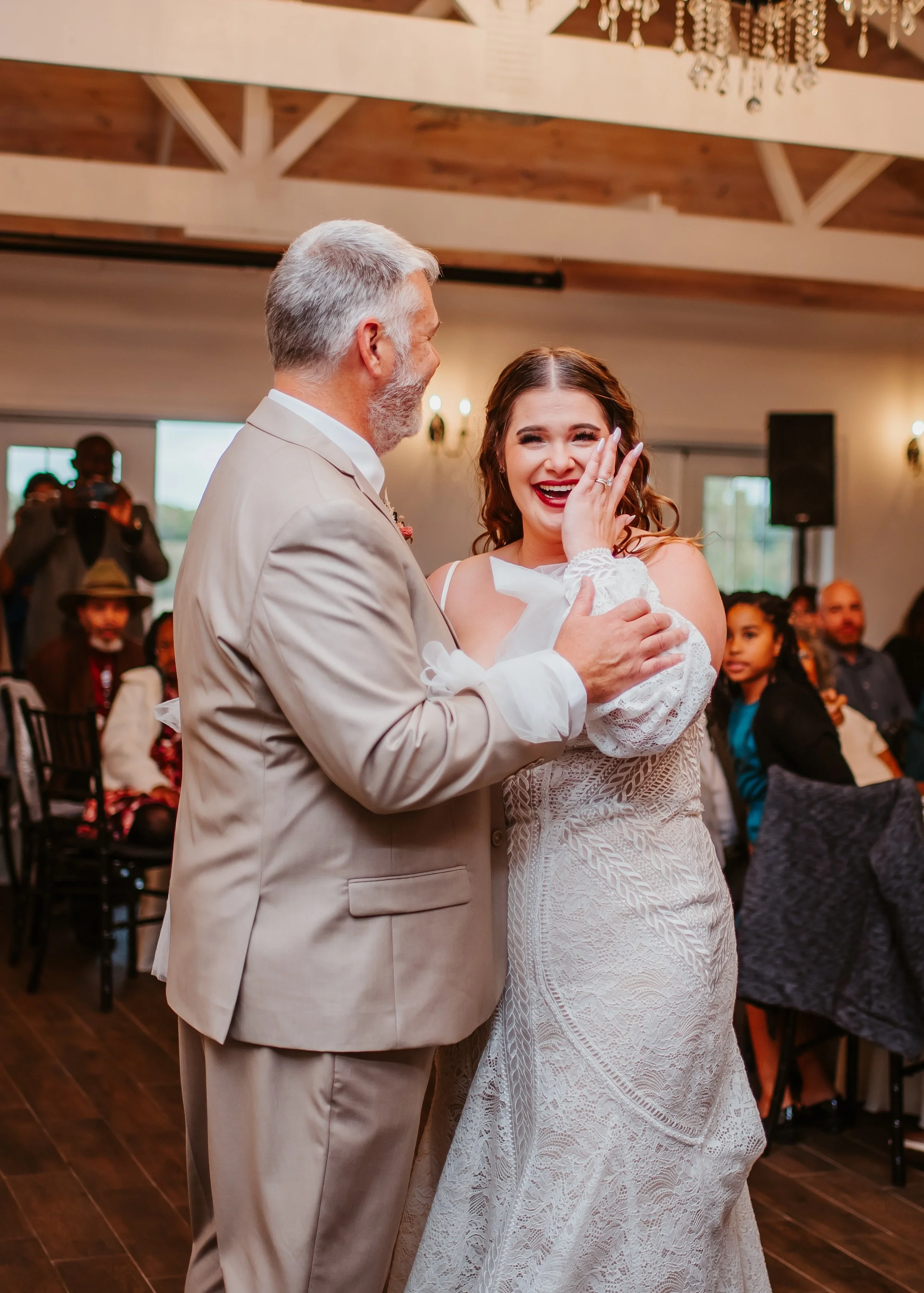 A joyful bride and groom dancing at their wedding reception, surrounded by guests seated at tables in a decorated hall.