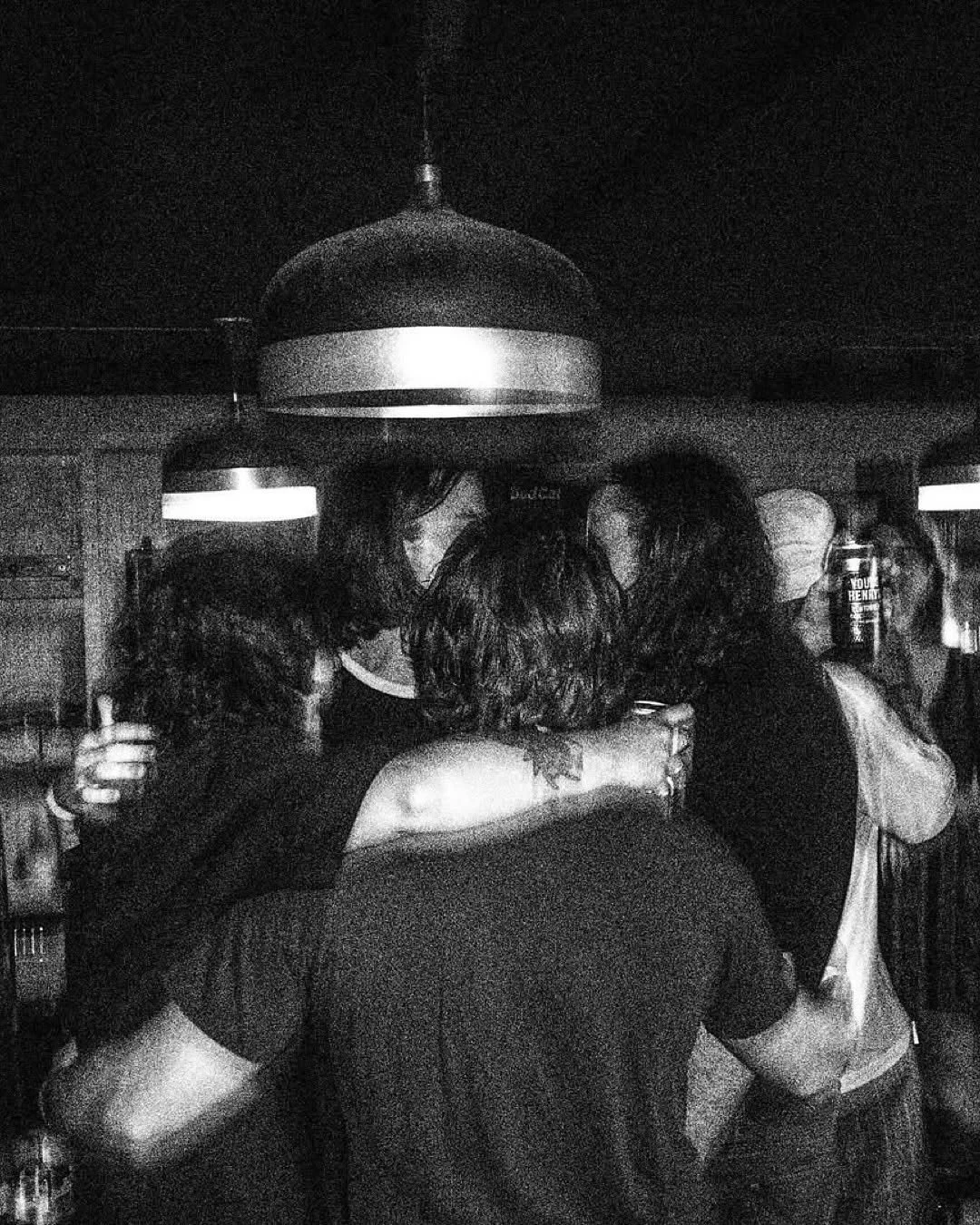 Group of people hugging in a dimly lit room with hanging lights.