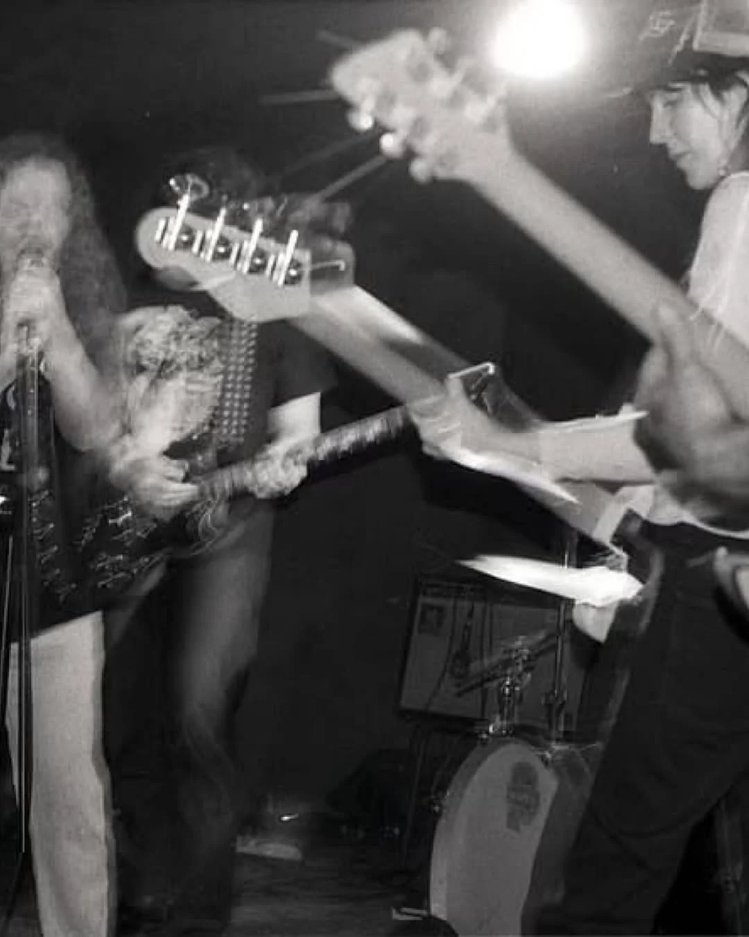 Two women playing music together; one is playing a bass guitar, and the other is playing an acoustic guitar and singing into a microphone.