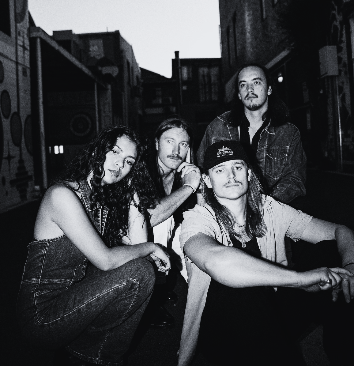 Five young adults posing outdoors at dusk, with urban buildings in the background.