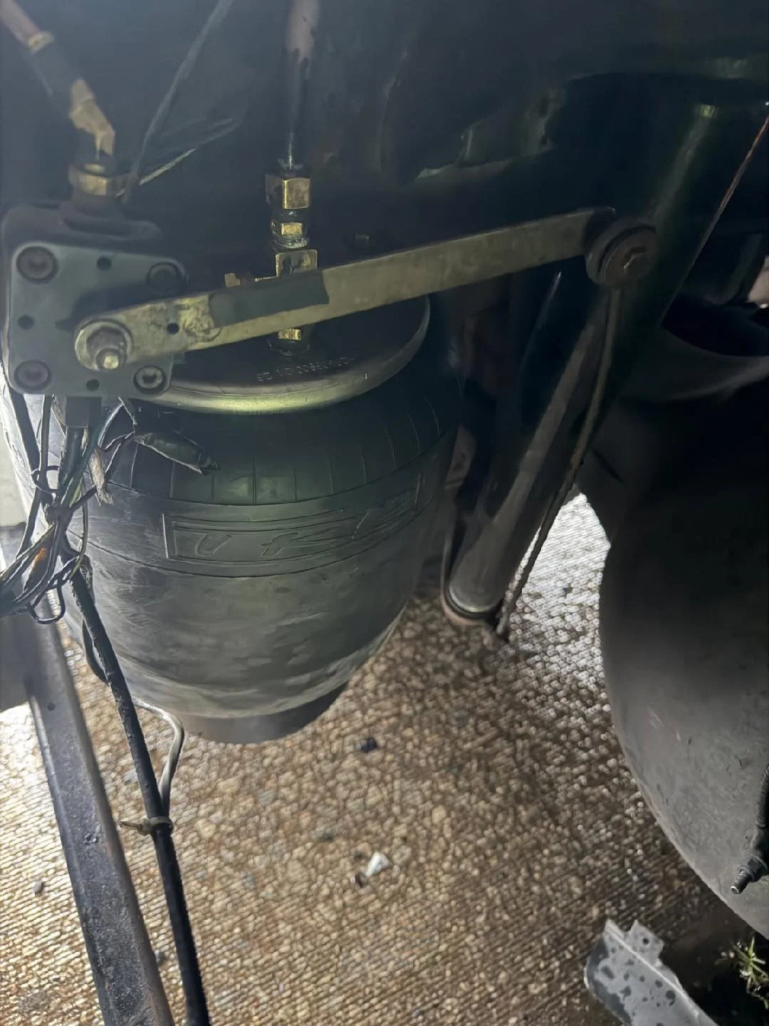 Close-up of a section of a mechanical or electronic device, showing metal components, cables, and a partially visible tire on a textured surface.