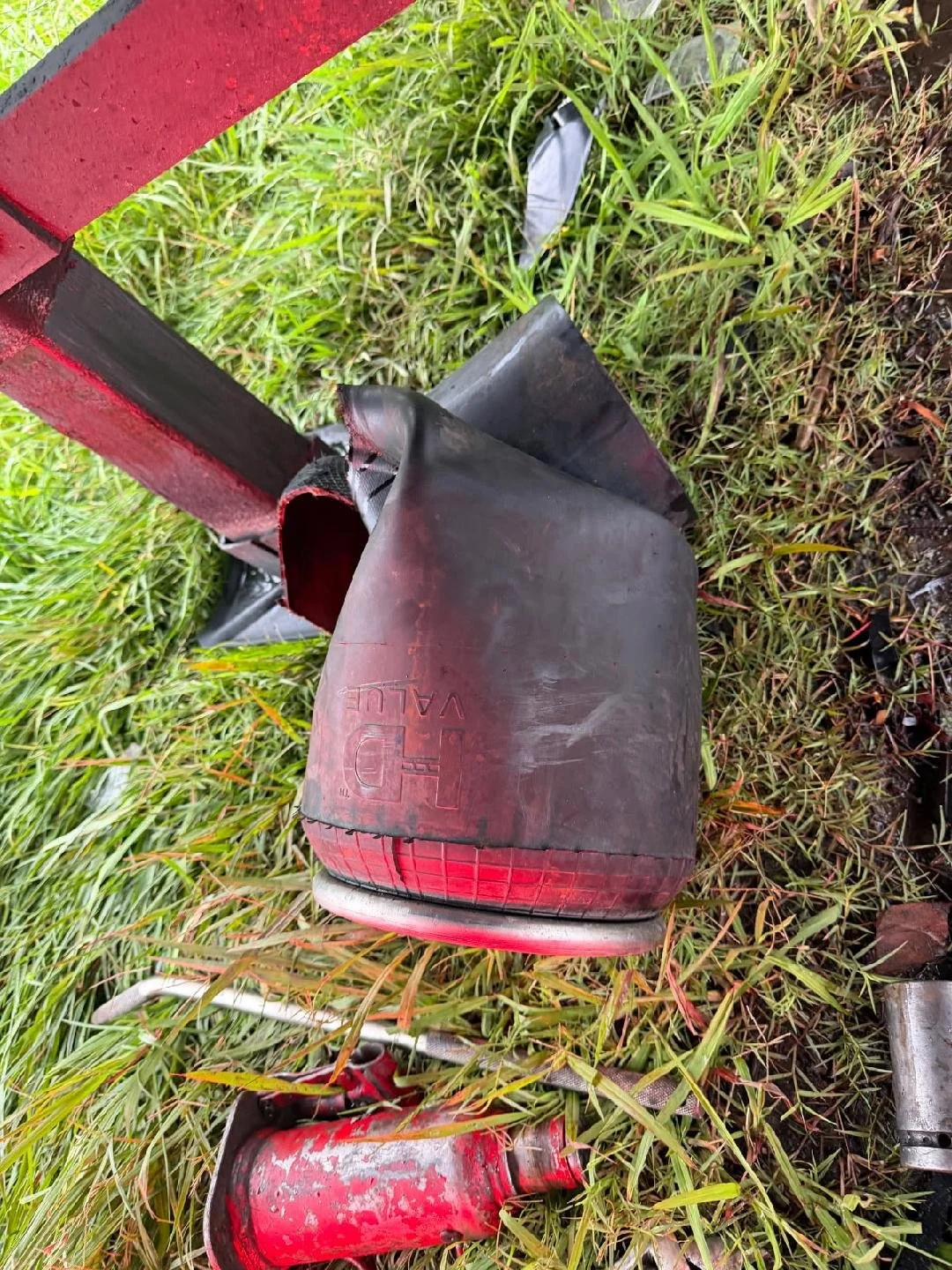Damaged black and red vehicle tail light on grass with parts of the vehicle's red frame visible.