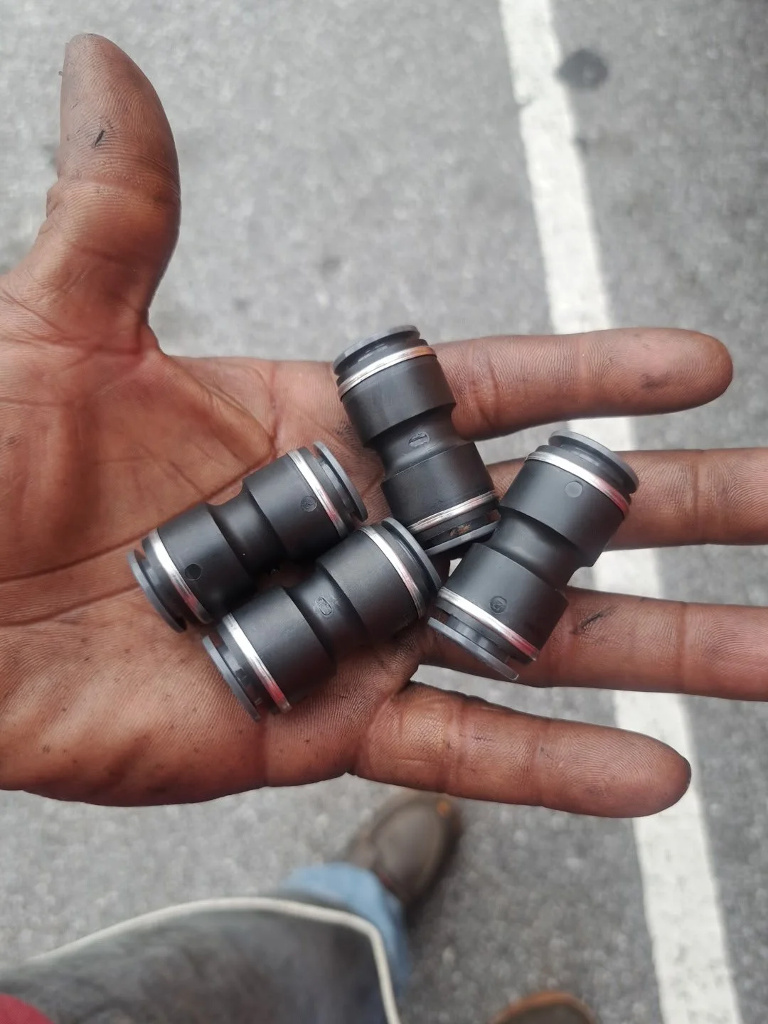 A person's hand holding five small black mechanical parts with red and silver rings on a gray pavement.