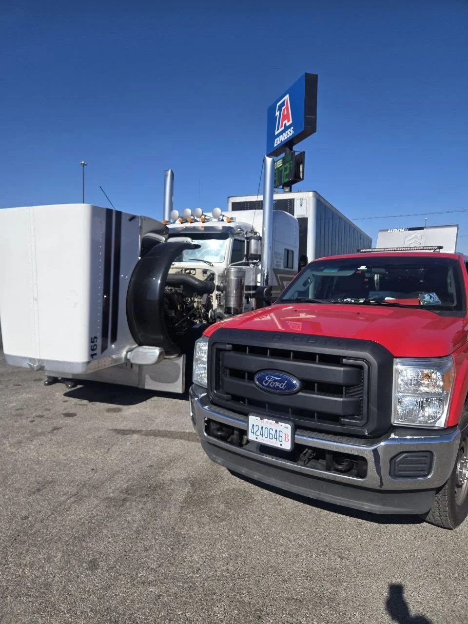 A red Ford truck parked at an Express gas station, with a semi-truck trailer behind it. The station sign displays the brand and a temperature of 72°F.