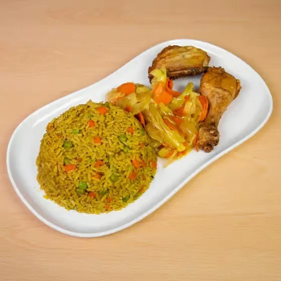 Plate of yellow rice with vegetables, a piece of cooked chicken drumstick, and a piece of roasted fish on a white oval dish.