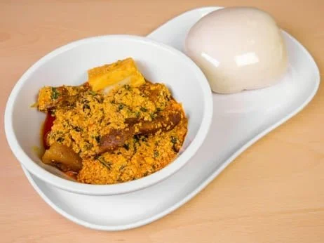 A white dish with a round mound of soft, white bread and a bowl of vegetable curry with turmeric, pumpkin, and other vegetables.