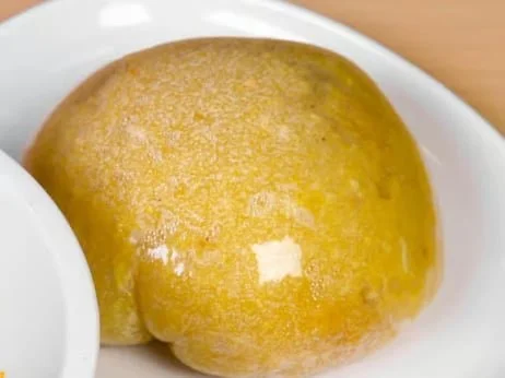 Close-up of a yellow, steamed bun on a white plate.