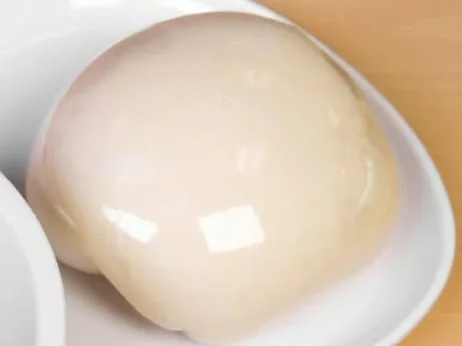 A round, white dessert on a white plate with a glossy surface.