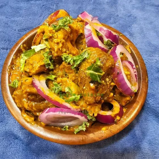 A wooden bowl filled with Indian curry, garnished with red onions and fresh cilantro, placed on a blue cloth.