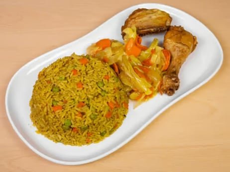 Plate of yellow rice with vegetables, fried chicken pieces, and cooked vegetables on a white oval plate.