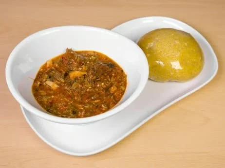 A white oval plate with two compartments: one containing a bowl of vegetable curry and the other holding a round, yellow mound of cooked food.