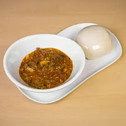A white tray with two compartments, one containing a boiled egg and the other holding a bowl of spicy soup.