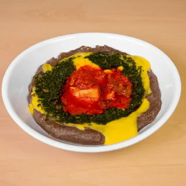 A bowl of Ash-e shooli, an Iranian soup with black eyed peas, topped with tomato sauce, herbs, and a drizzle of yellow oil.