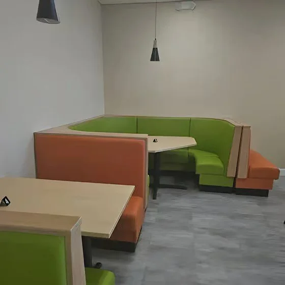 Corner booth seating with green and orange upholstery in a modern interior with gray flooring.