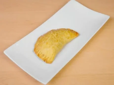 A single fried food item, possibly a potato wedge or fried snack, on a white paper towel placed on a wooden surface.